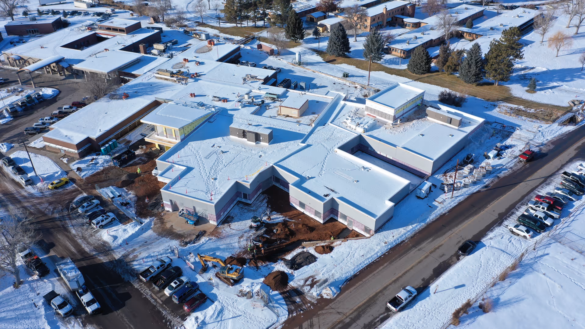 Snowy aerial view of a cross-shaped senior living facility with parked cars.