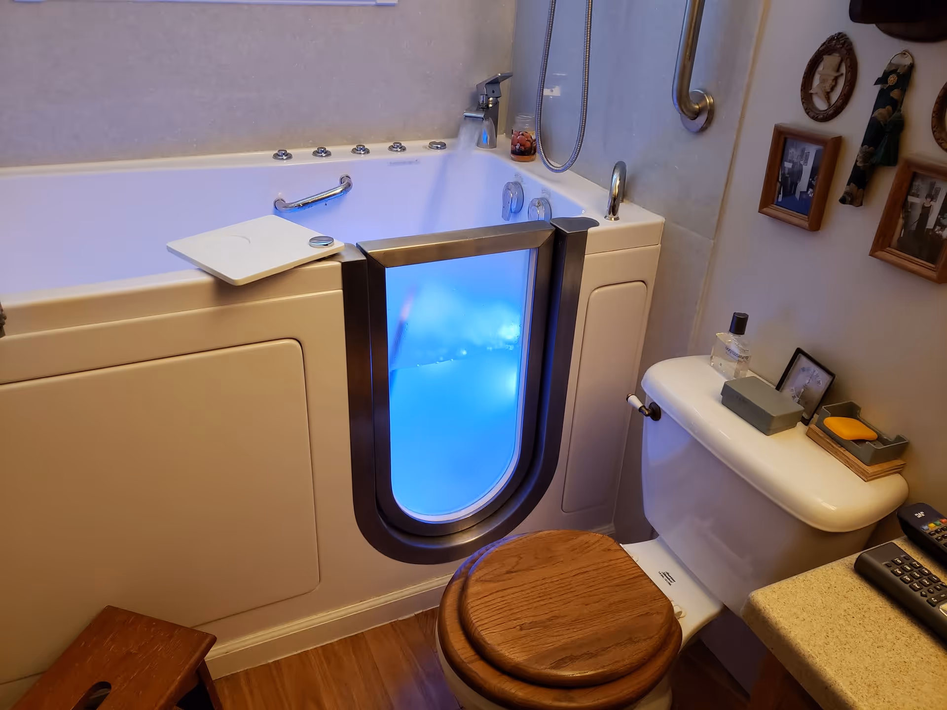Interior bathroom with a walk-in tub, blue-lit glass door, and nearby toilet.