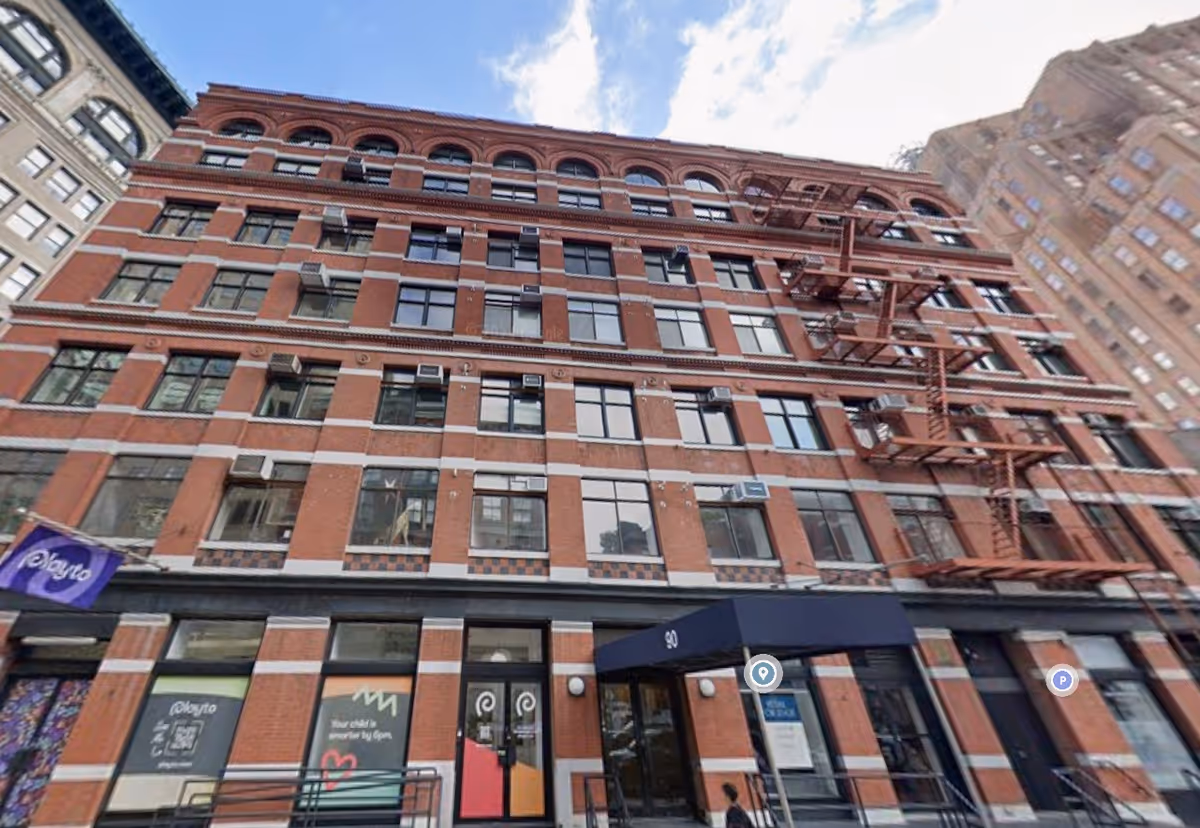 Brick urban building with red fire escapes and storefronts along a busy city street.