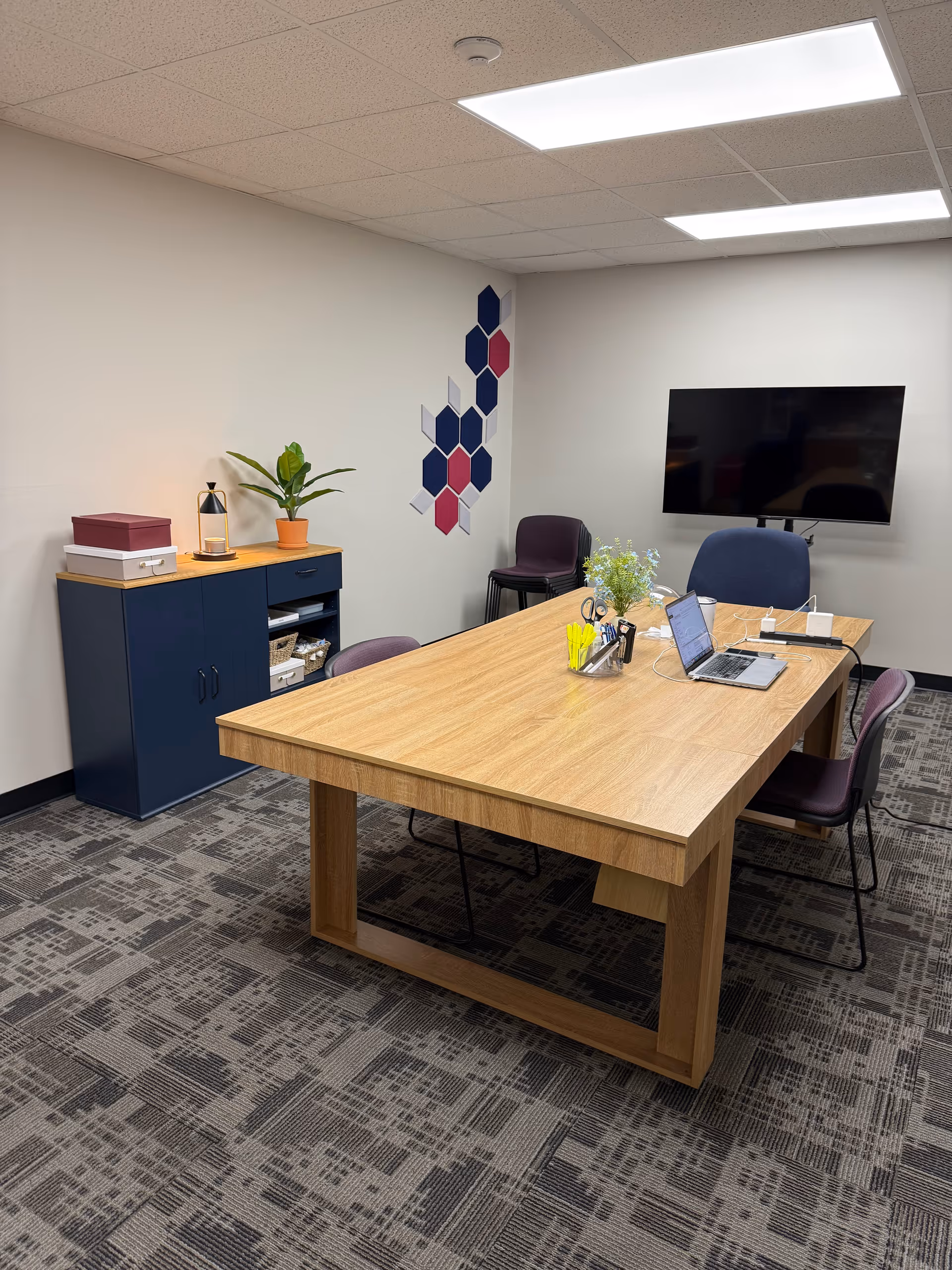 An empty senior living facility conference area with a wooden table, chairs, plant, and TV.