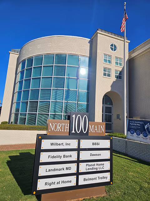Front view of a brick building with curved glass facade and directory sign.