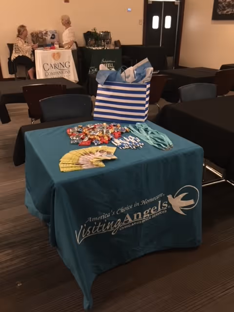 Indoor event hall with a Visiting Angels table and two attendees in background.