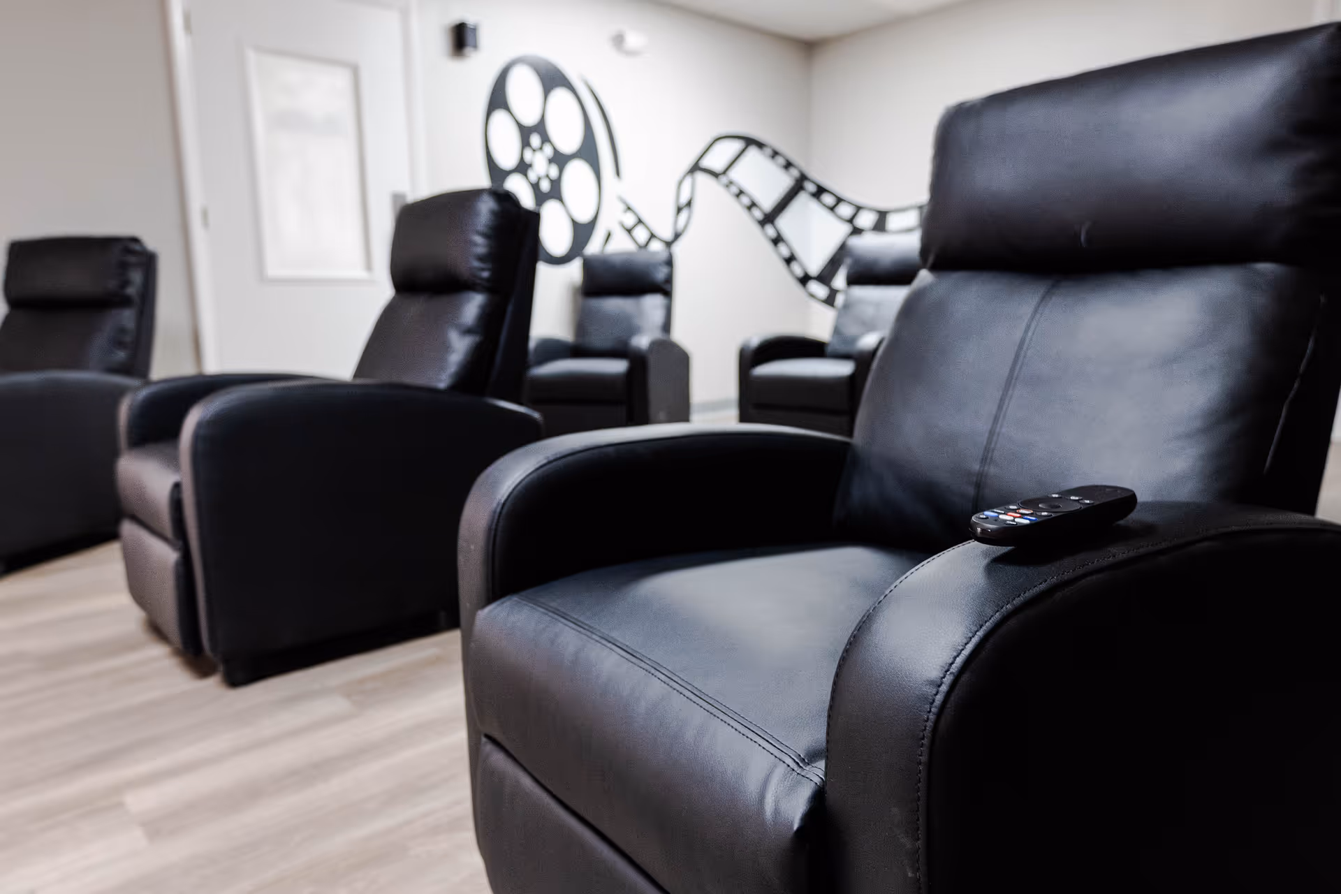 Cinema lounge featuring black leather recliners and film reel wall art.