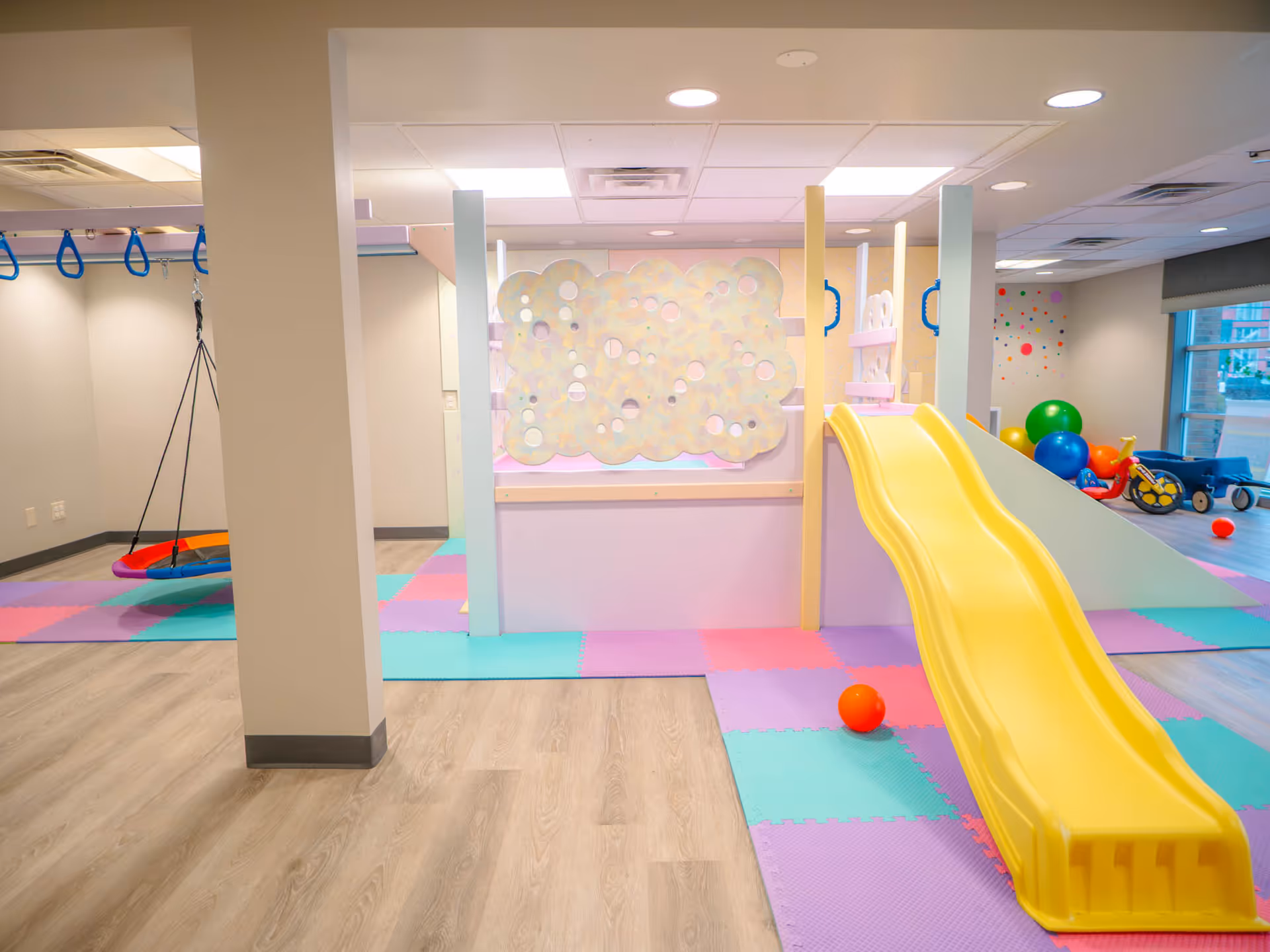 Colorful indoor play area with a yellow slide, foam mats, and climbing structure.