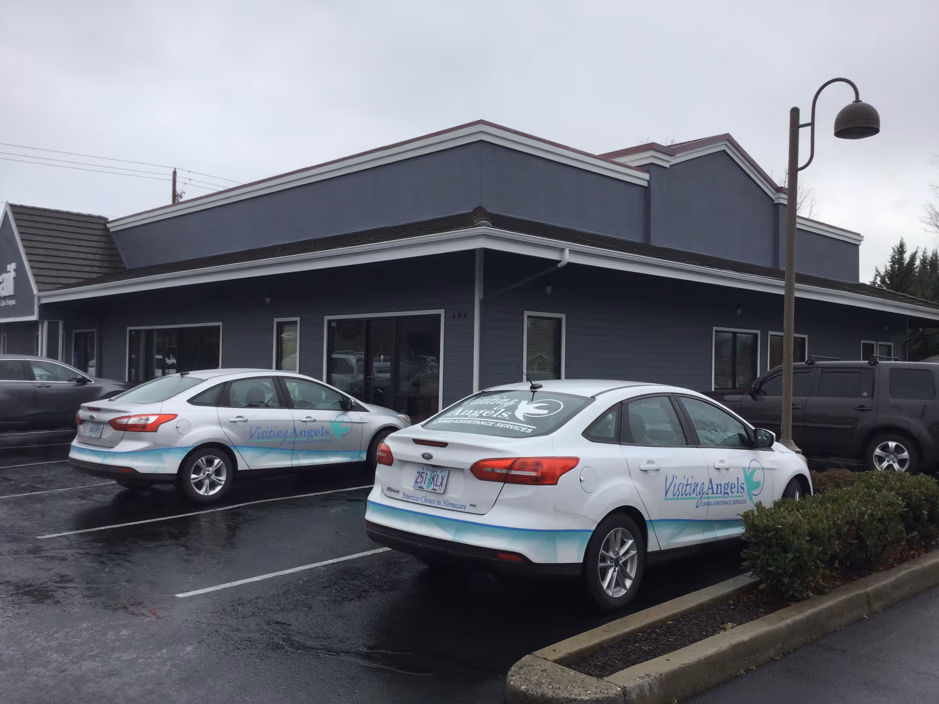 Exterior view of Visiting Angels facility with two branded cars parked in front.