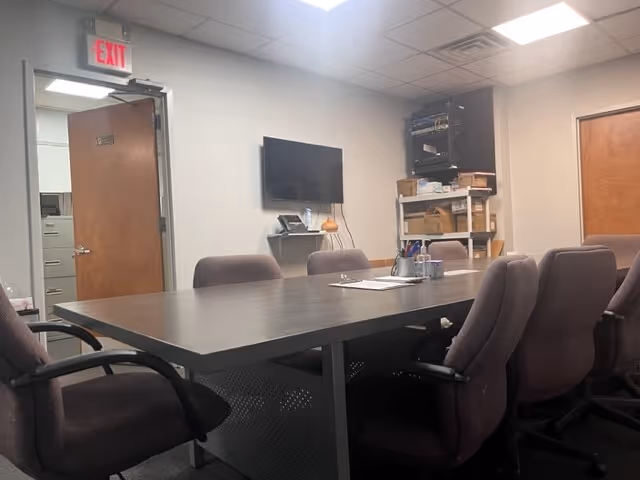 A conference room with a long table, purple chairs, a wall TV, and shelving.
