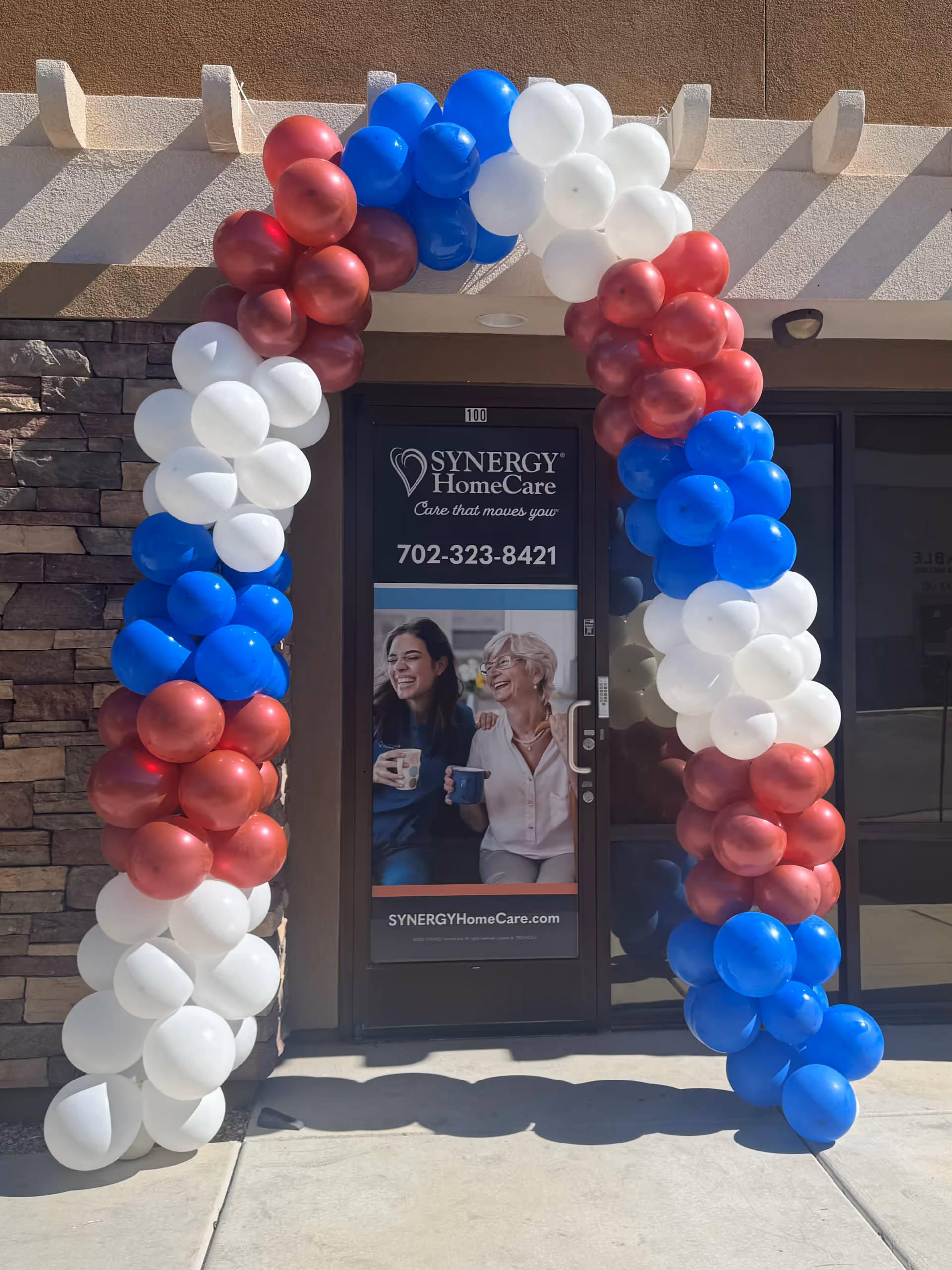 Entrance to Synergy HomeCare with a large red, white, and blue balloon arch.