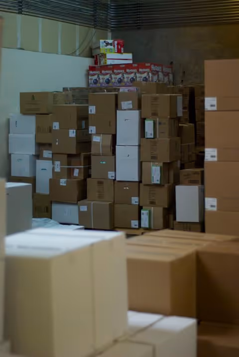 A dim storage room with tall stacks of cardboard boxes and assorted packaging.