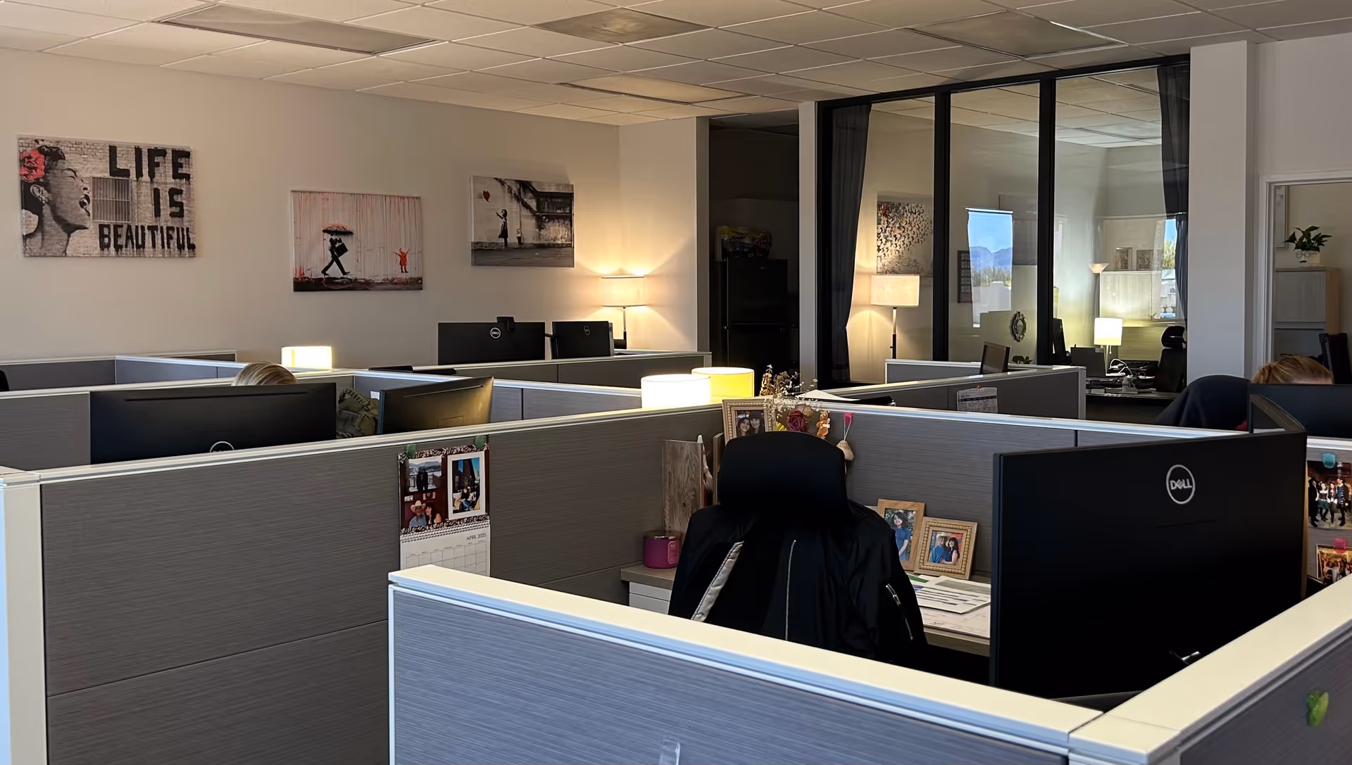 Open office cubicles with computers, photos, and soft lighting in a corporate workspace.