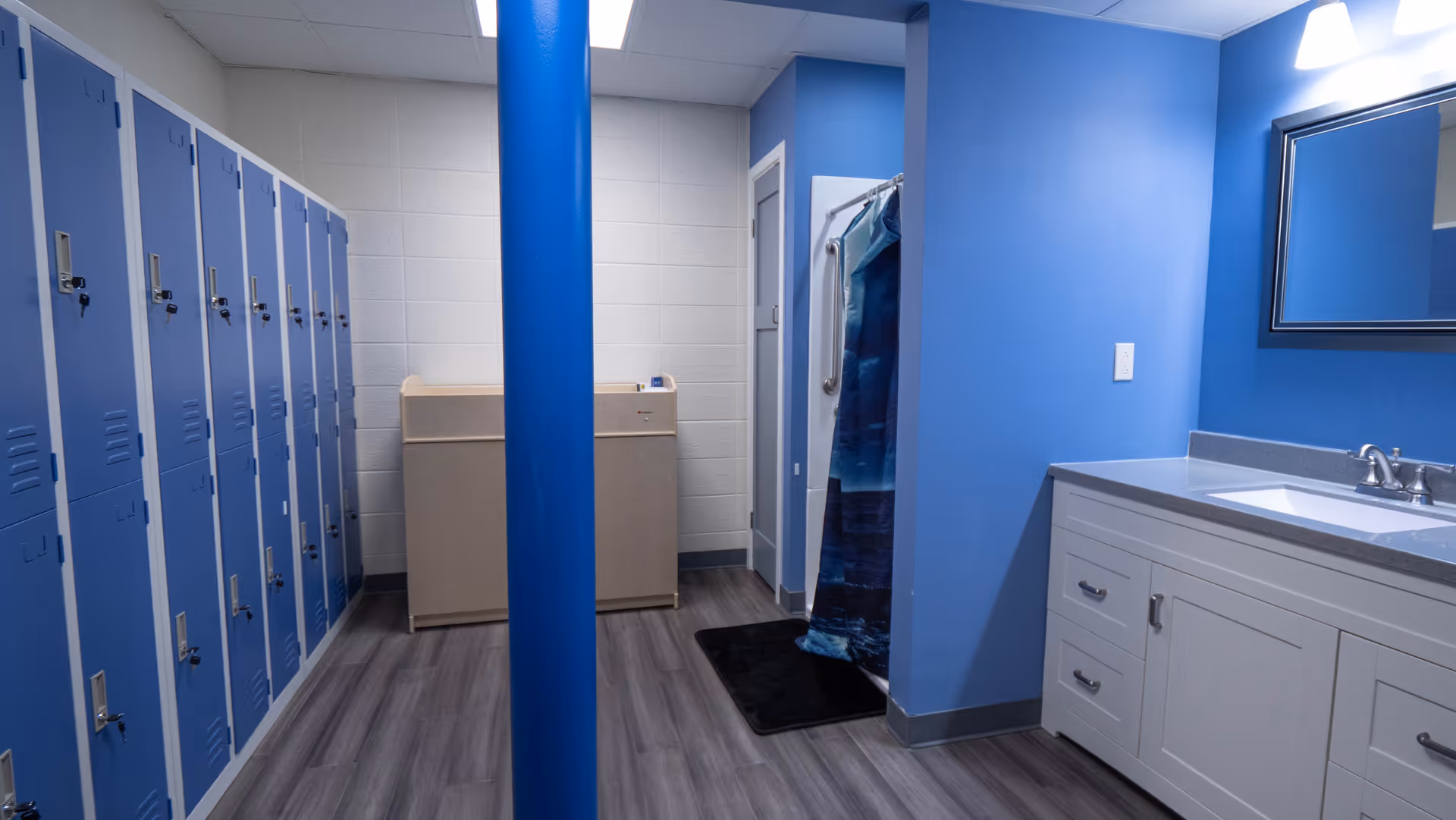 Blue lockers line a hallway with a laundry unit, blue pillar, and bathroom vanity.