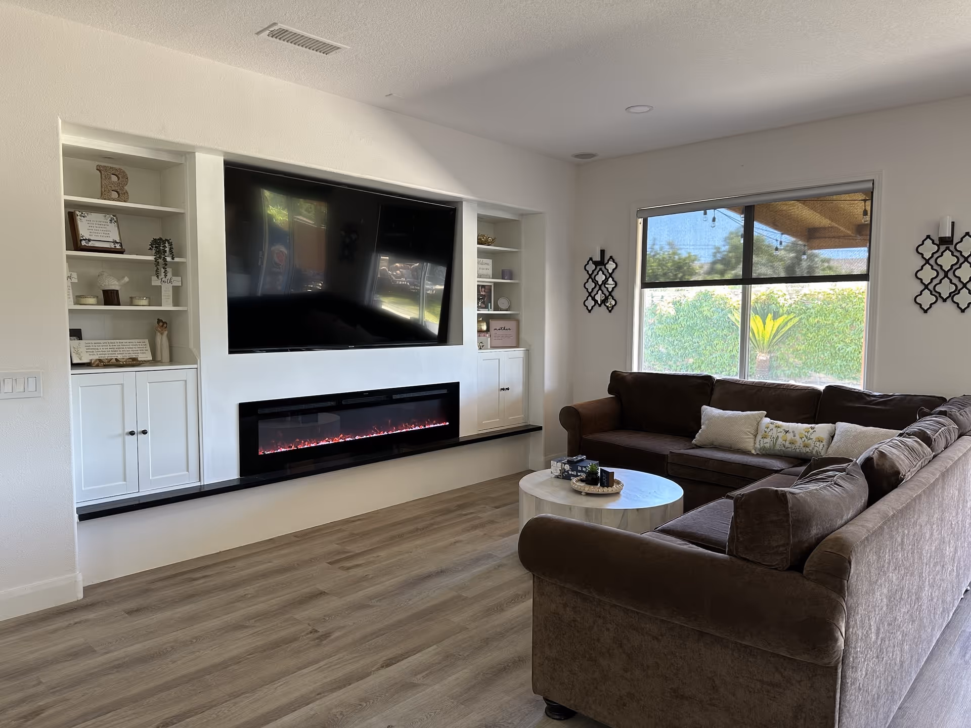 Bright living room with built-in shelves, TV, electric fireplace, and brown sectional.