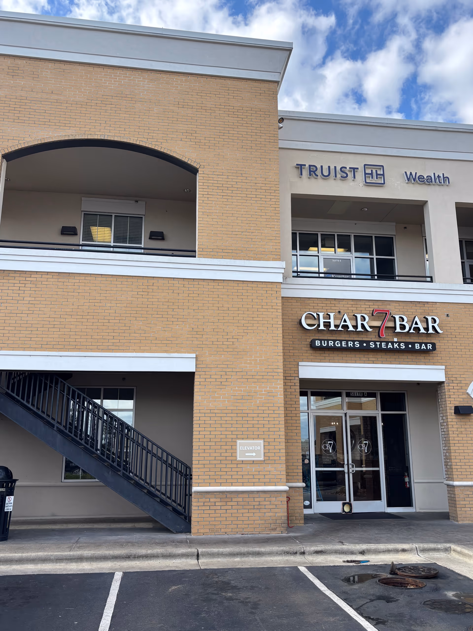 Exterior view of a brick shopping center with Char7 Bar and Trust Wealth signage.