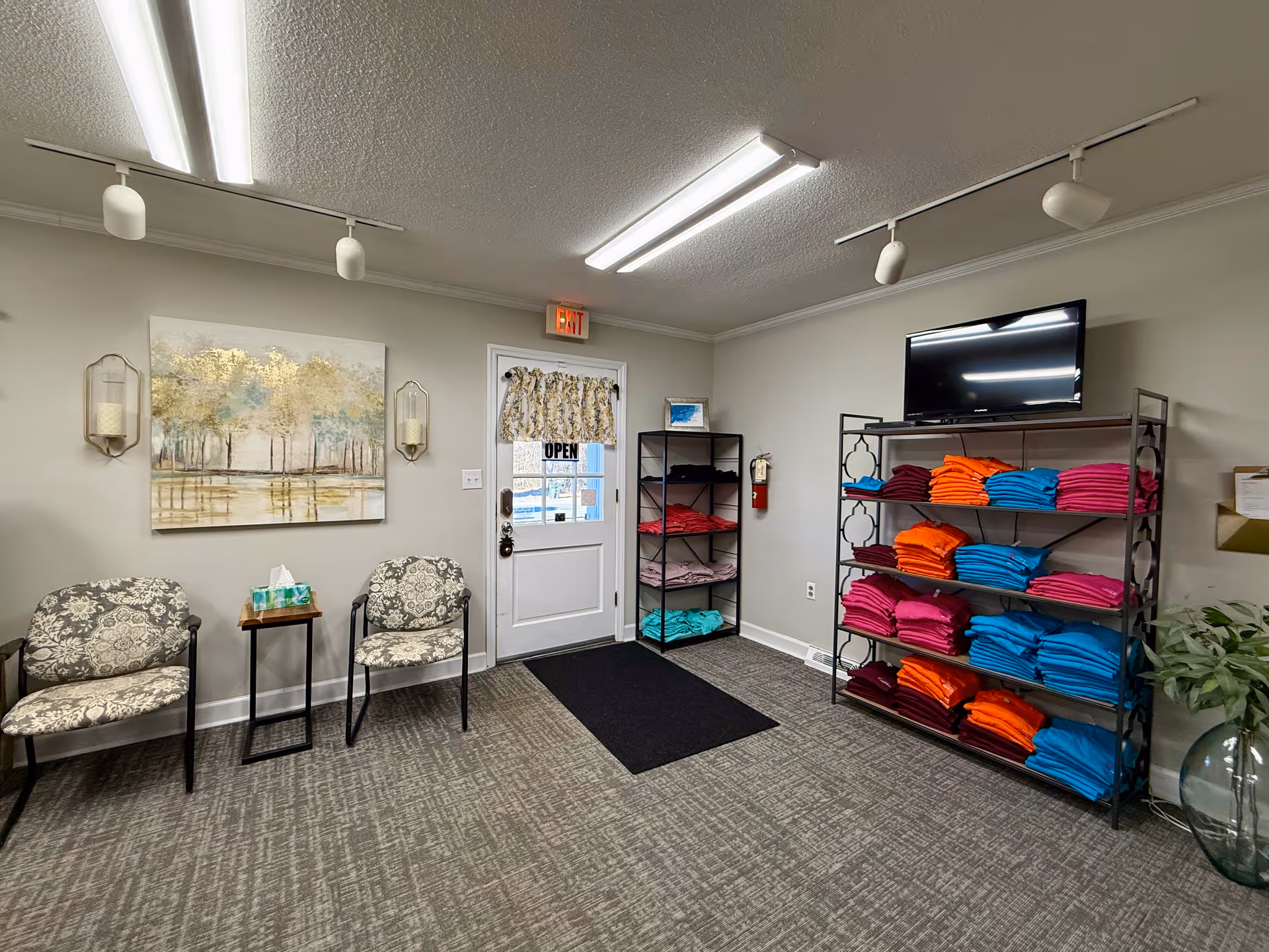 A waiting area inside a senior care facility with patterned chairs, shelves of colorful folded towels.