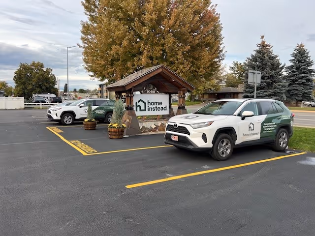 Home Instead service vehicles parked near a covered entrance with autumn trees.