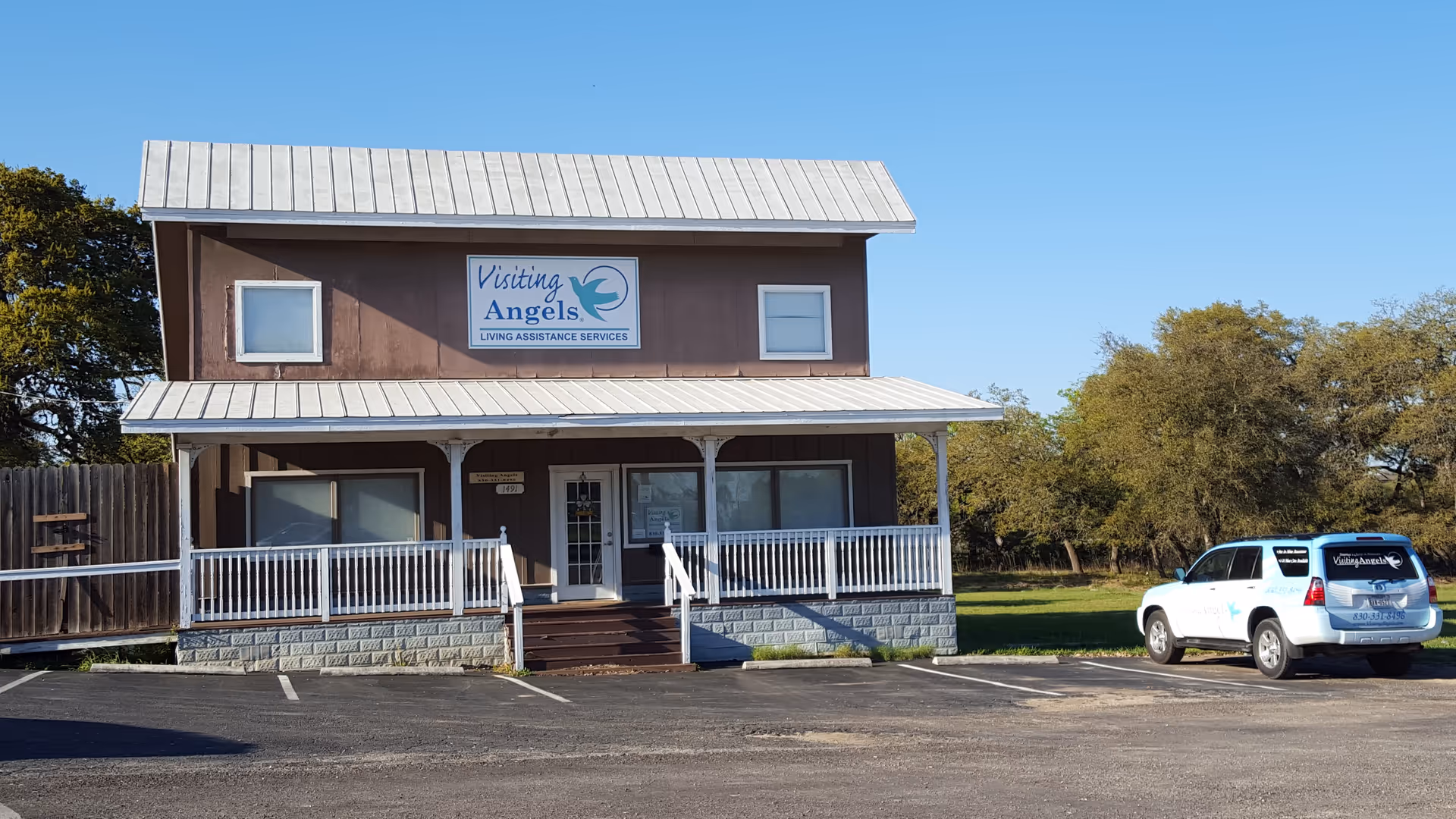 Two-story brown senior home care building with a Visiting Angels sign and parked white SUV.
