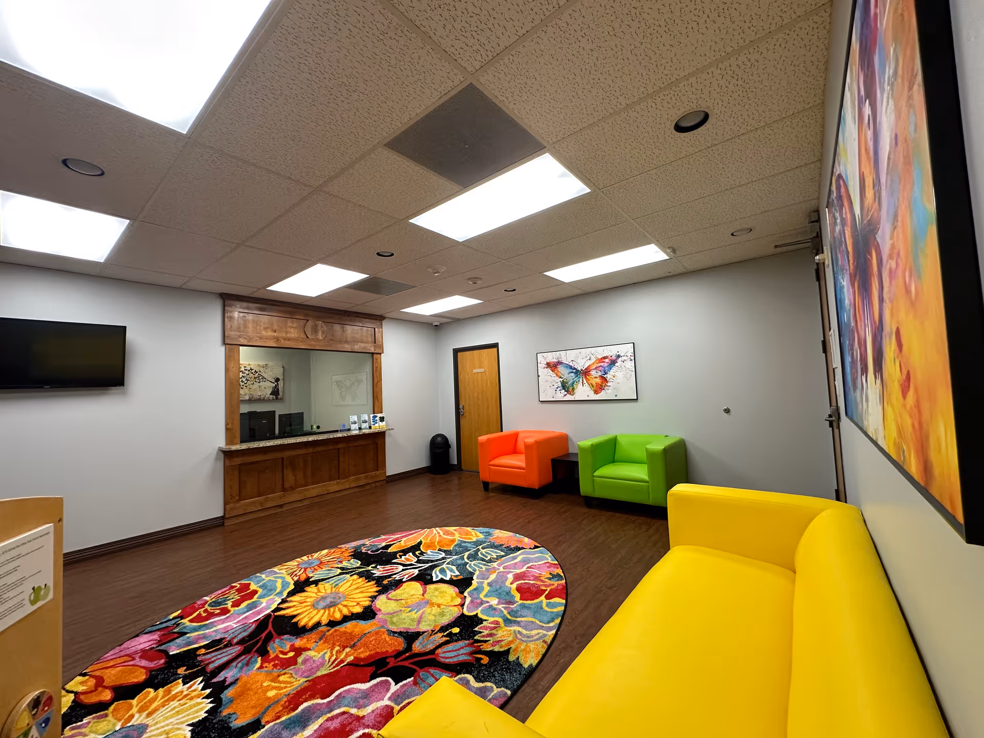Bright interior lounge with colorful chairs, a wooden reception counter, and butterfly artwork.