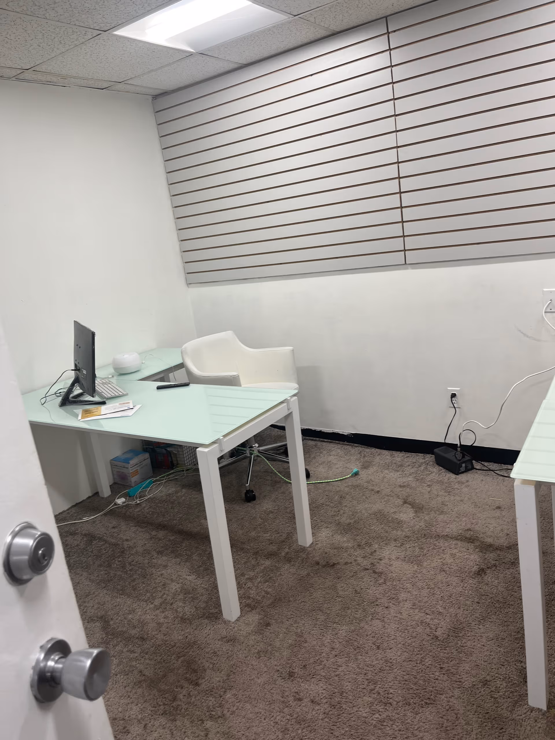 Small office space with two glass desks, a computer, and white chairs.