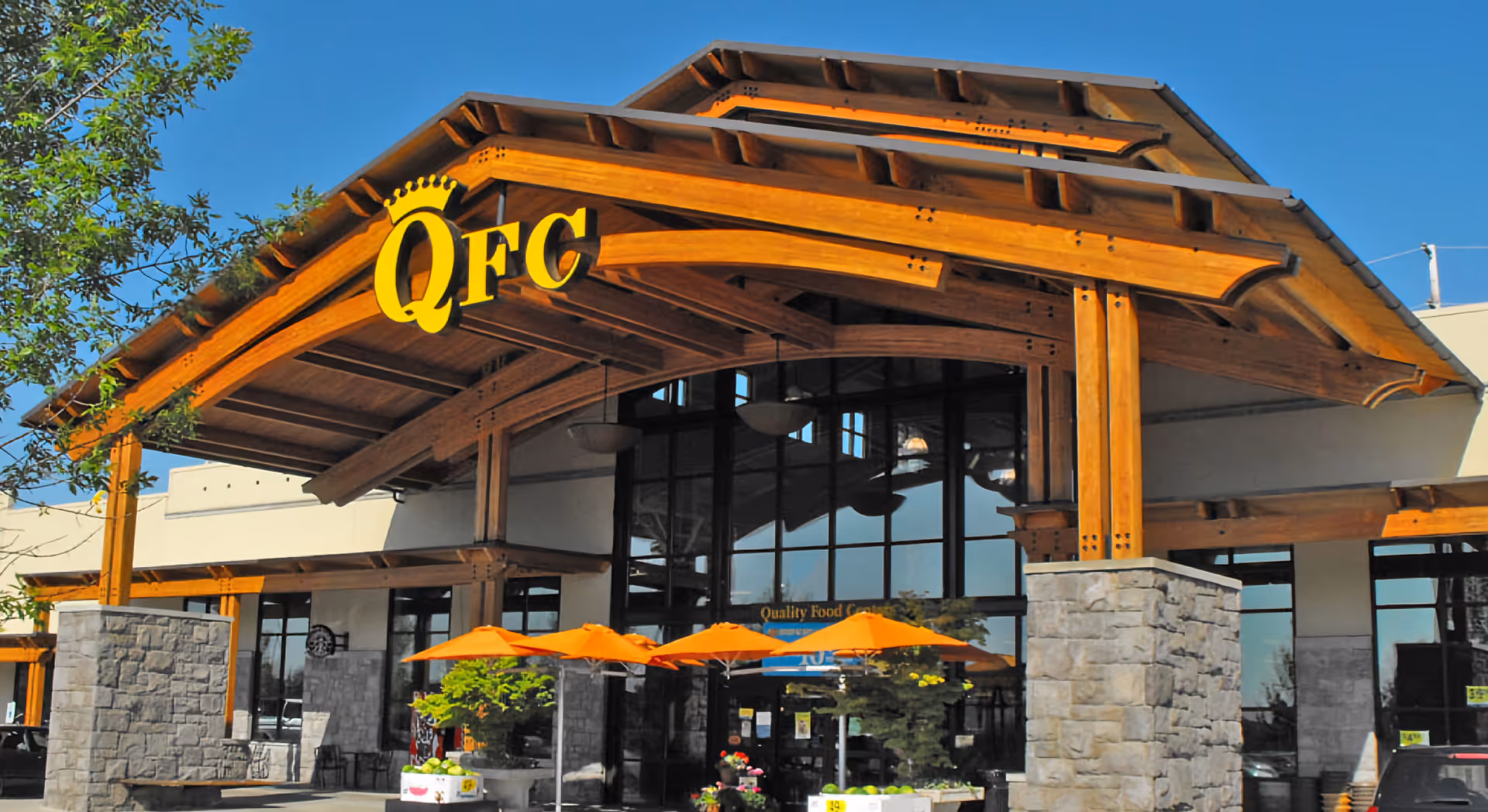 Exterior of QFC Pharmacy storefront with wooden arch and orange umbrellas.