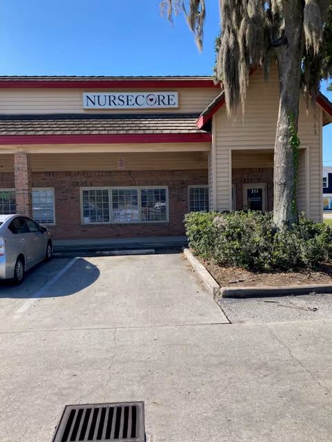 Exterior view of NurseCore facility with sign, parking area, and surrounding shrubs.