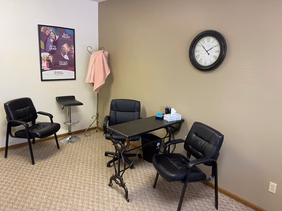 An interior office area with black chairs, a desk, clock, and pink coat on a stand.