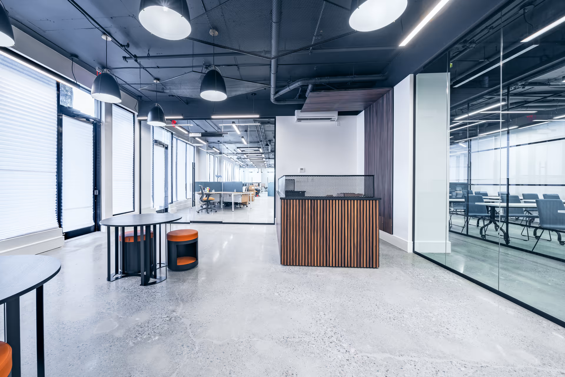 Modern reception area with a wooden front desk, glass walls, and seating in an open lobby.