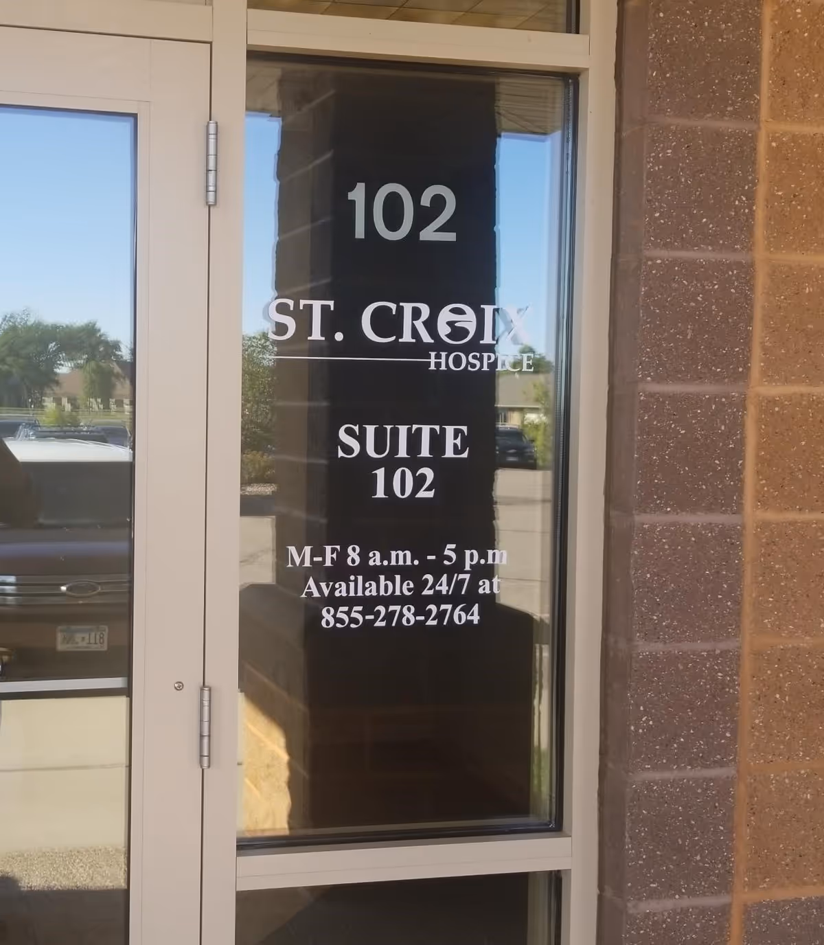 Glass door with 102 suite signage and hospice contact information on a brick exterior.