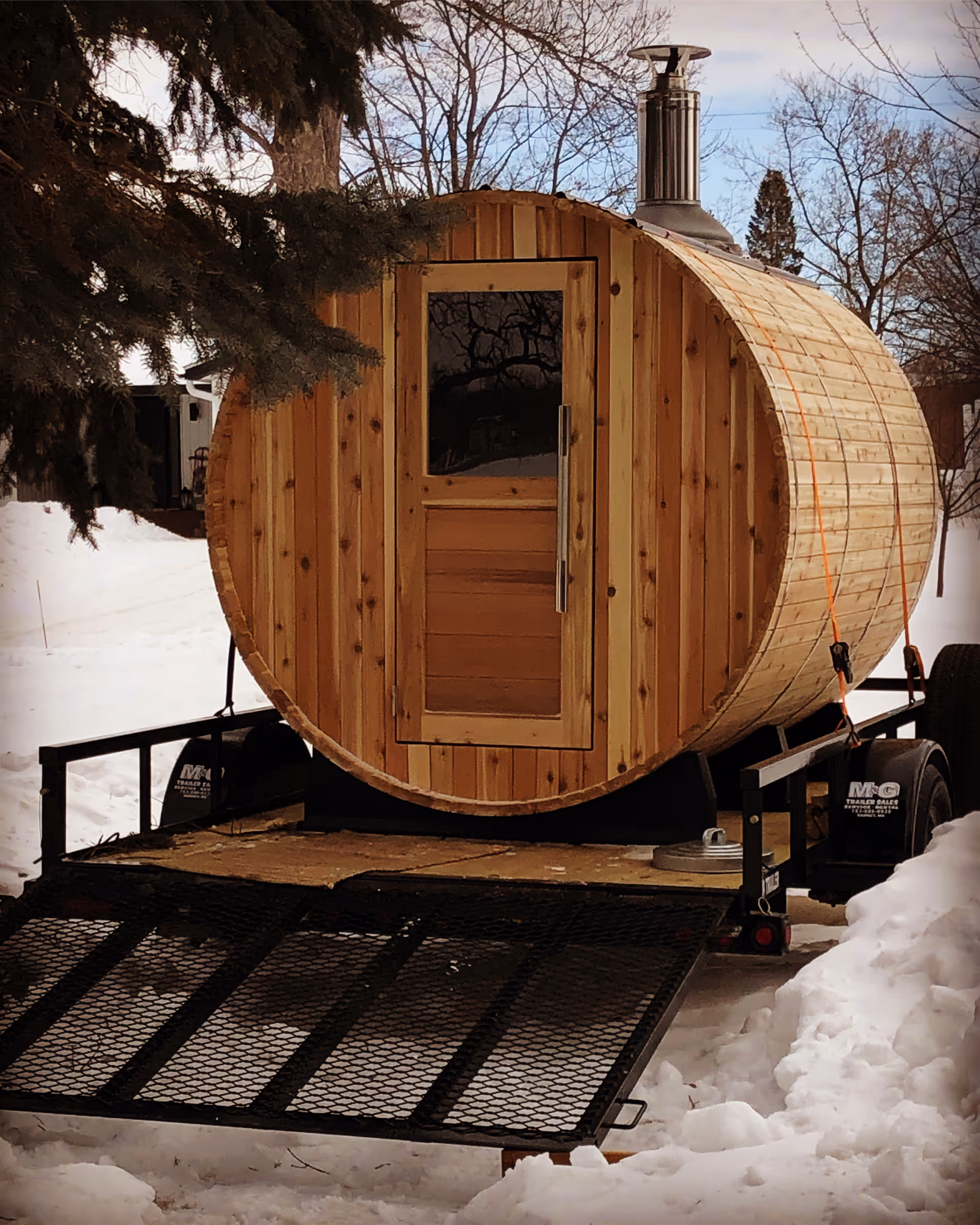 A wooden barrel sauna on a trailer sits outside in the snow.