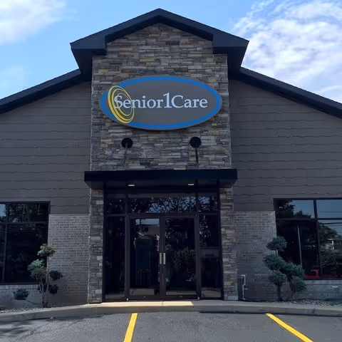 Front view of Senior1Care facility with stone facade, glass doors, and an oval sign.