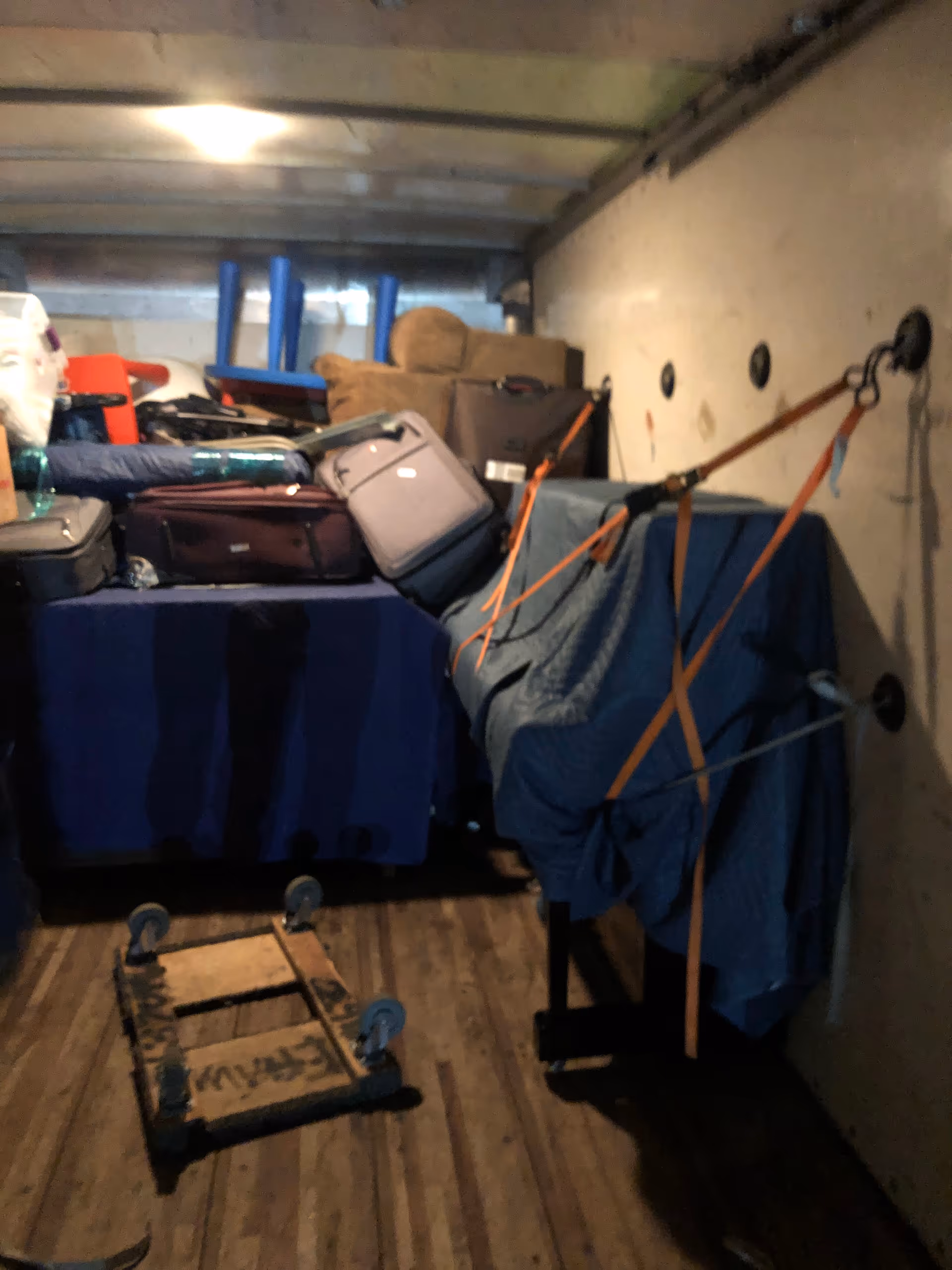 Dim storage area with stacked luggage and covered items in a cramped trailer.