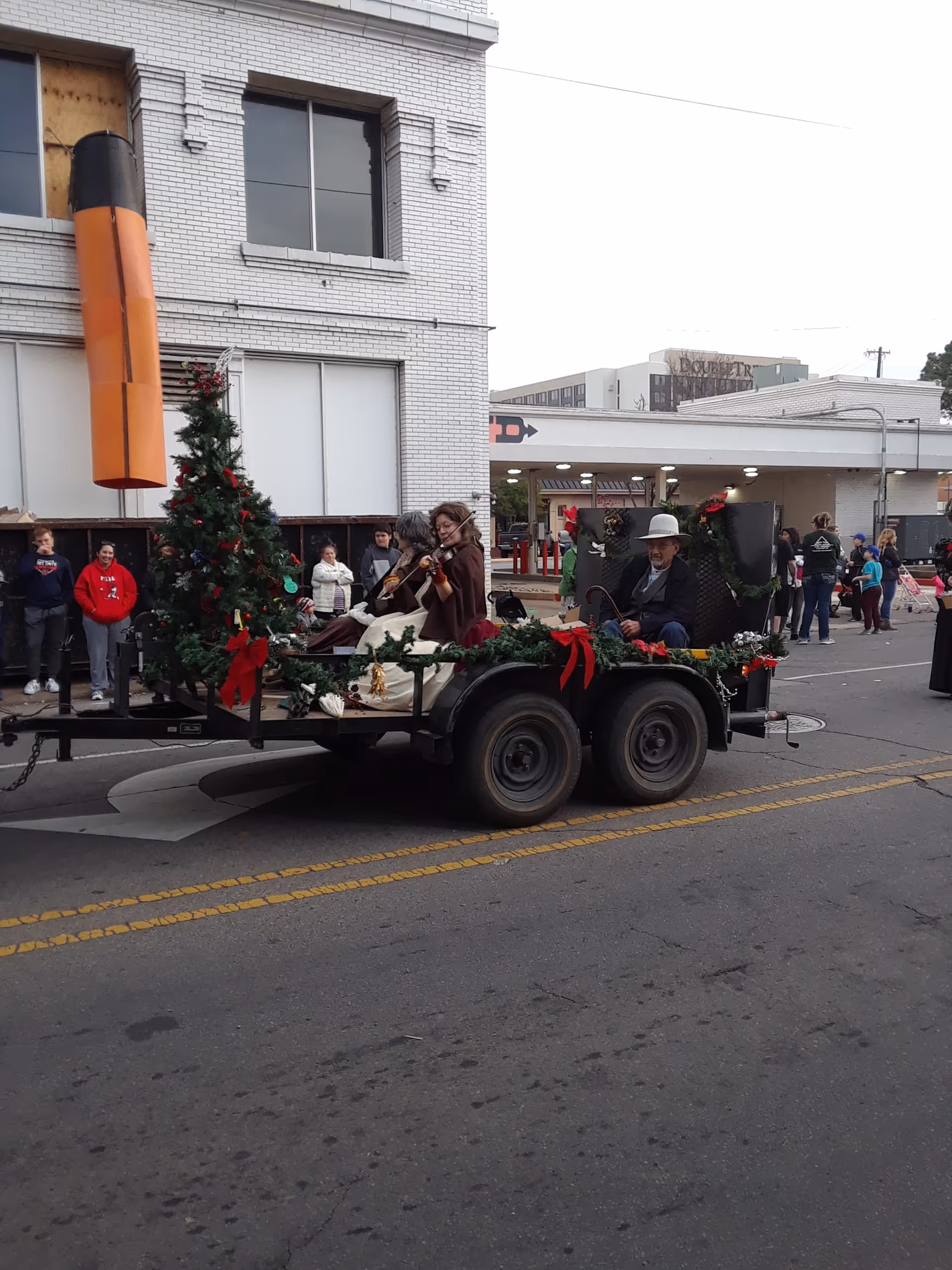 Decorated parade trailer with musicians and spectators along a city street