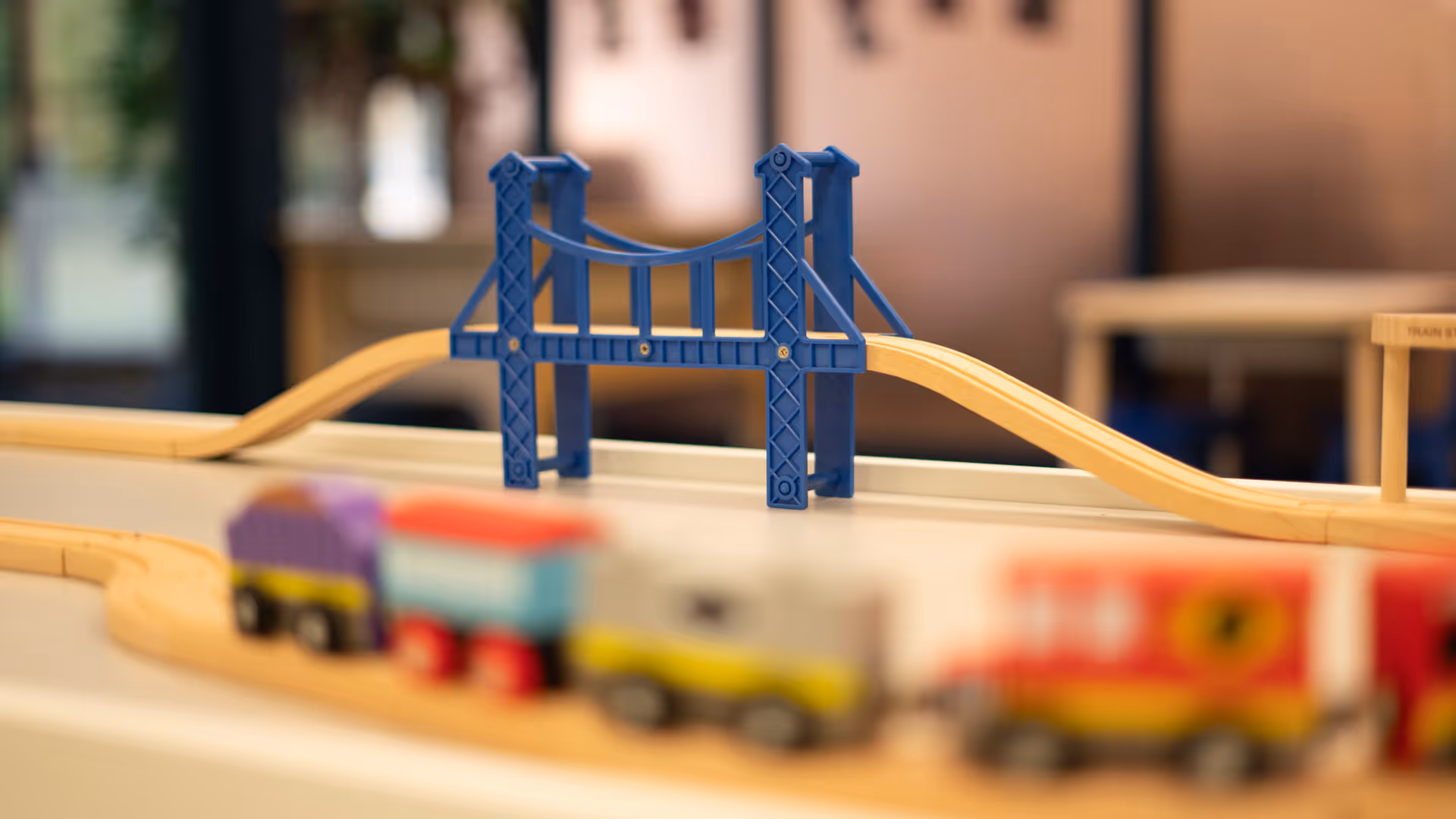 Indoor play area with a wooden train set and a blue bridge on a table.