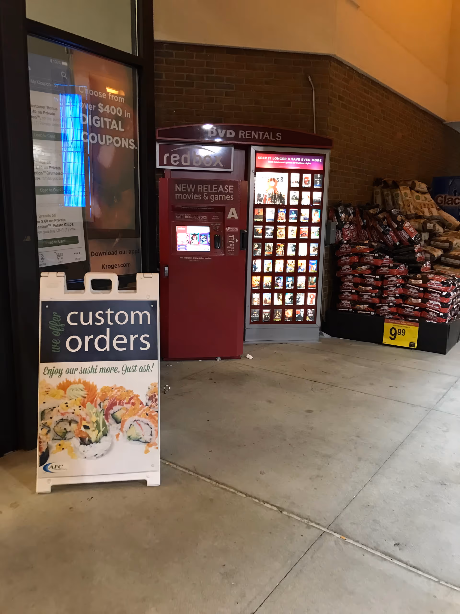 Storefront exterior with vending machines, a sushi sign, and a display board.