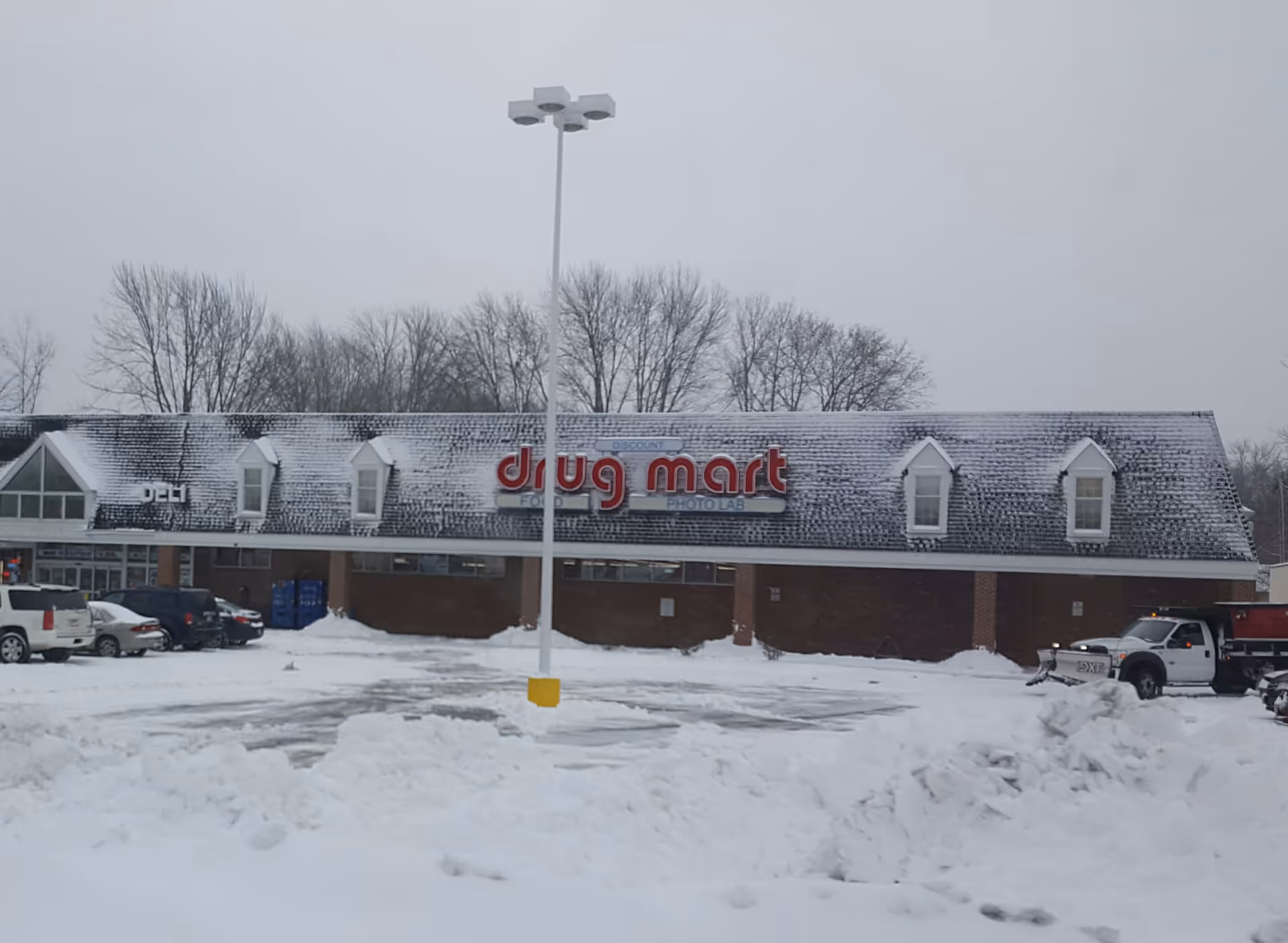Snow-covered Discount Drug Mart storefront with parked cars in a snowy lot