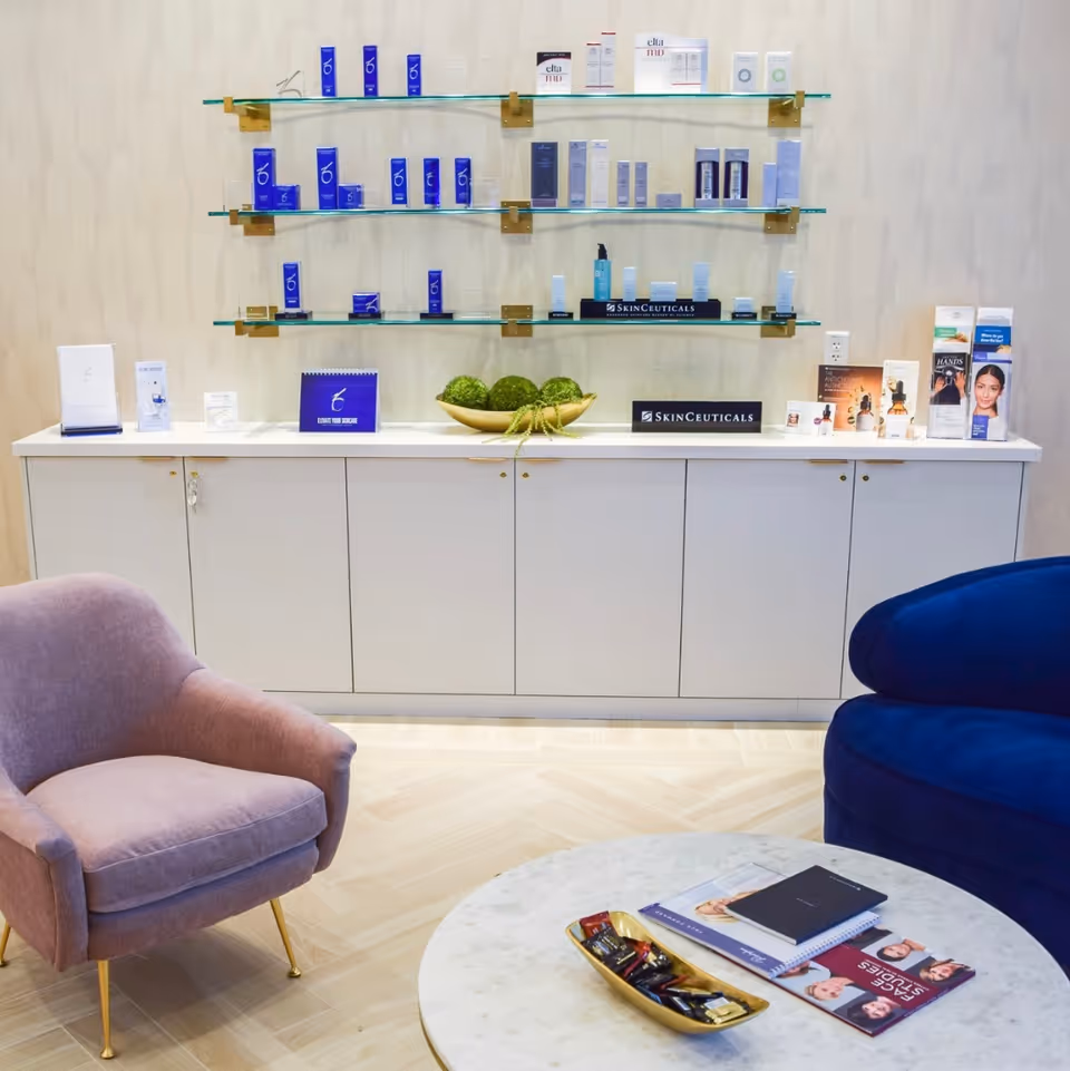 A skincare product display on glass shelves above white cabinets, with pink and blue lounge chairs.