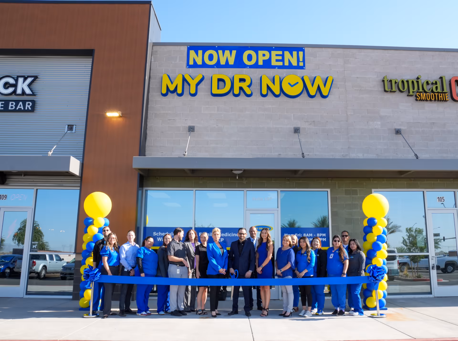 Staff members stand in front of a NOW OPEN MY DR NOW storefront with balloons.
