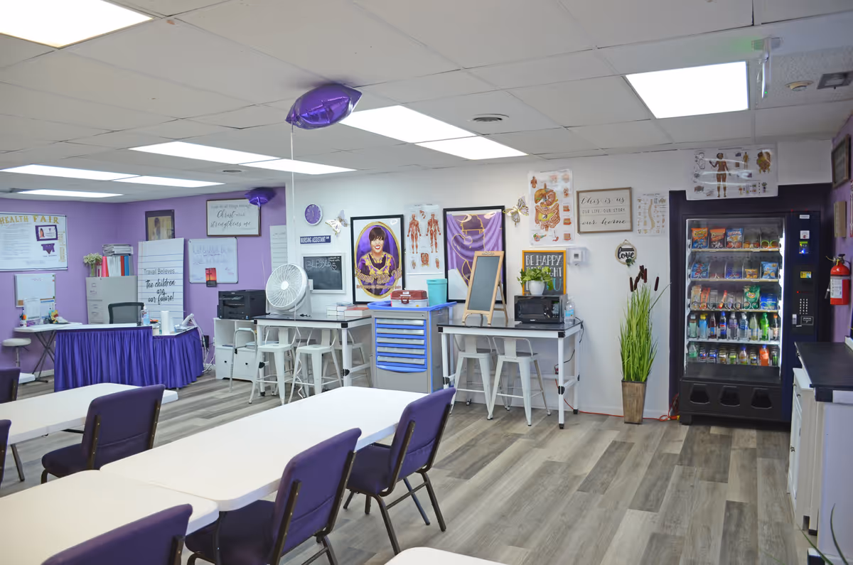Purple-accented community room with tables, chairs, bulletin boards, vending machine, and activity stations.