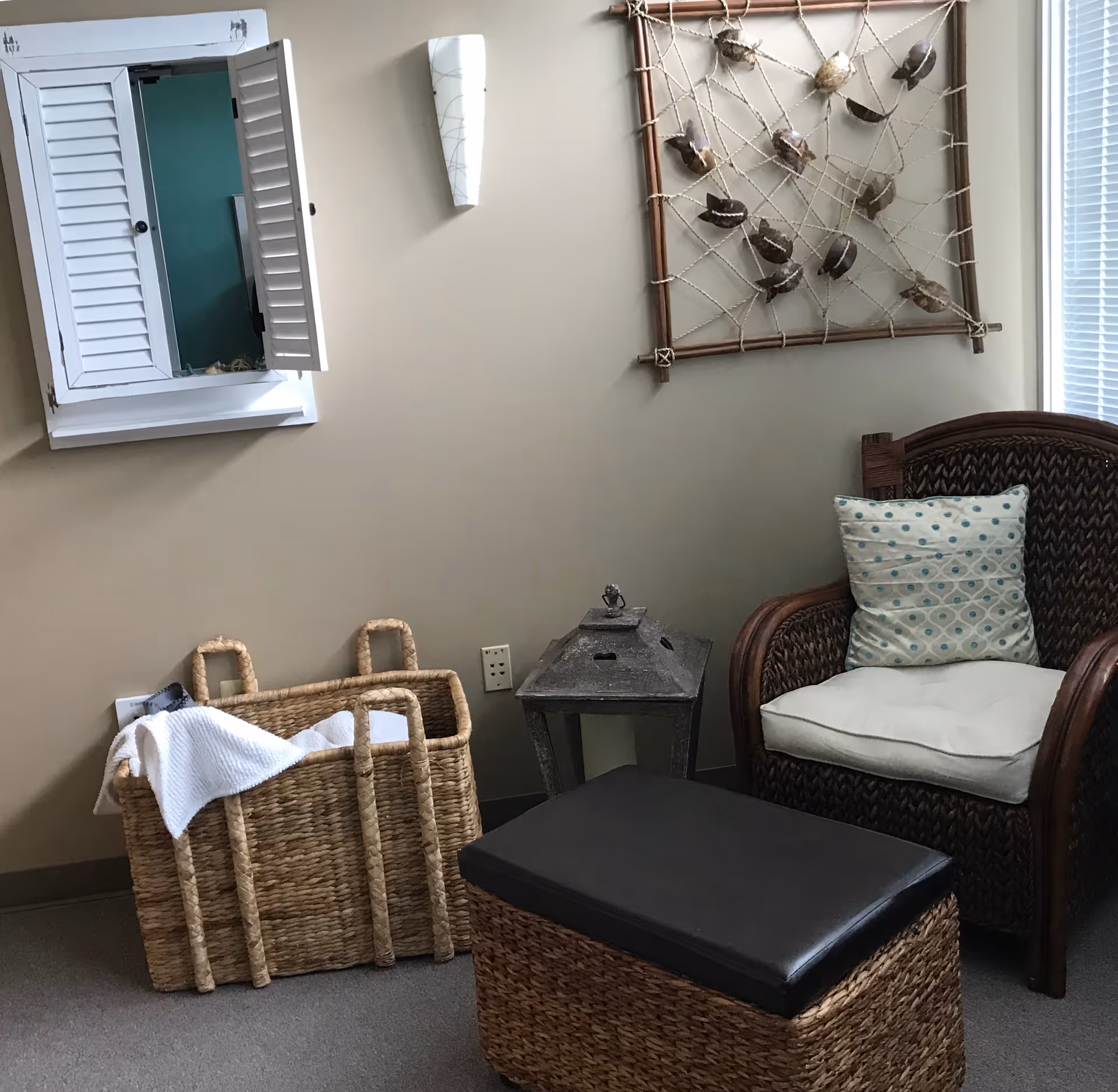 Cozy seating corner with wicker chair, ottoman, basket, and wall art.