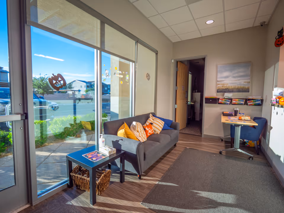 Bright lounge area with a gray sofa, cushions, and large windows.