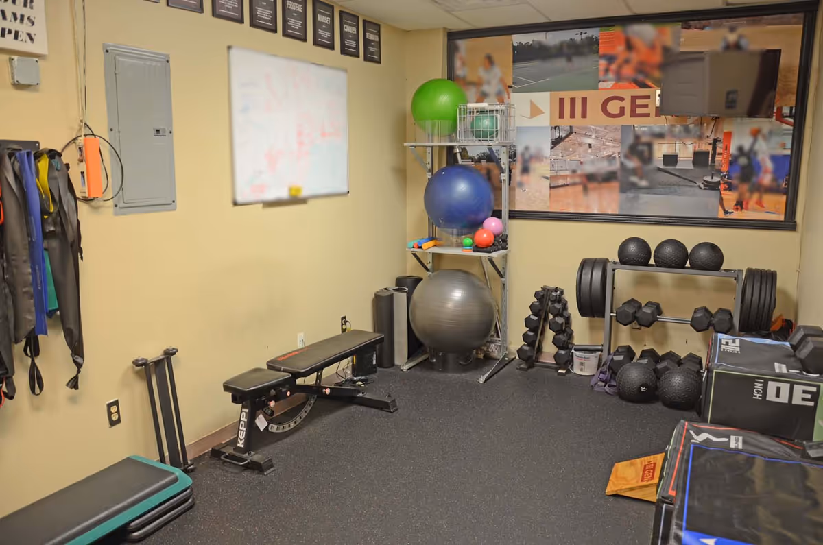 Compact gym room with bench, weights, medicine balls, and stability balls.