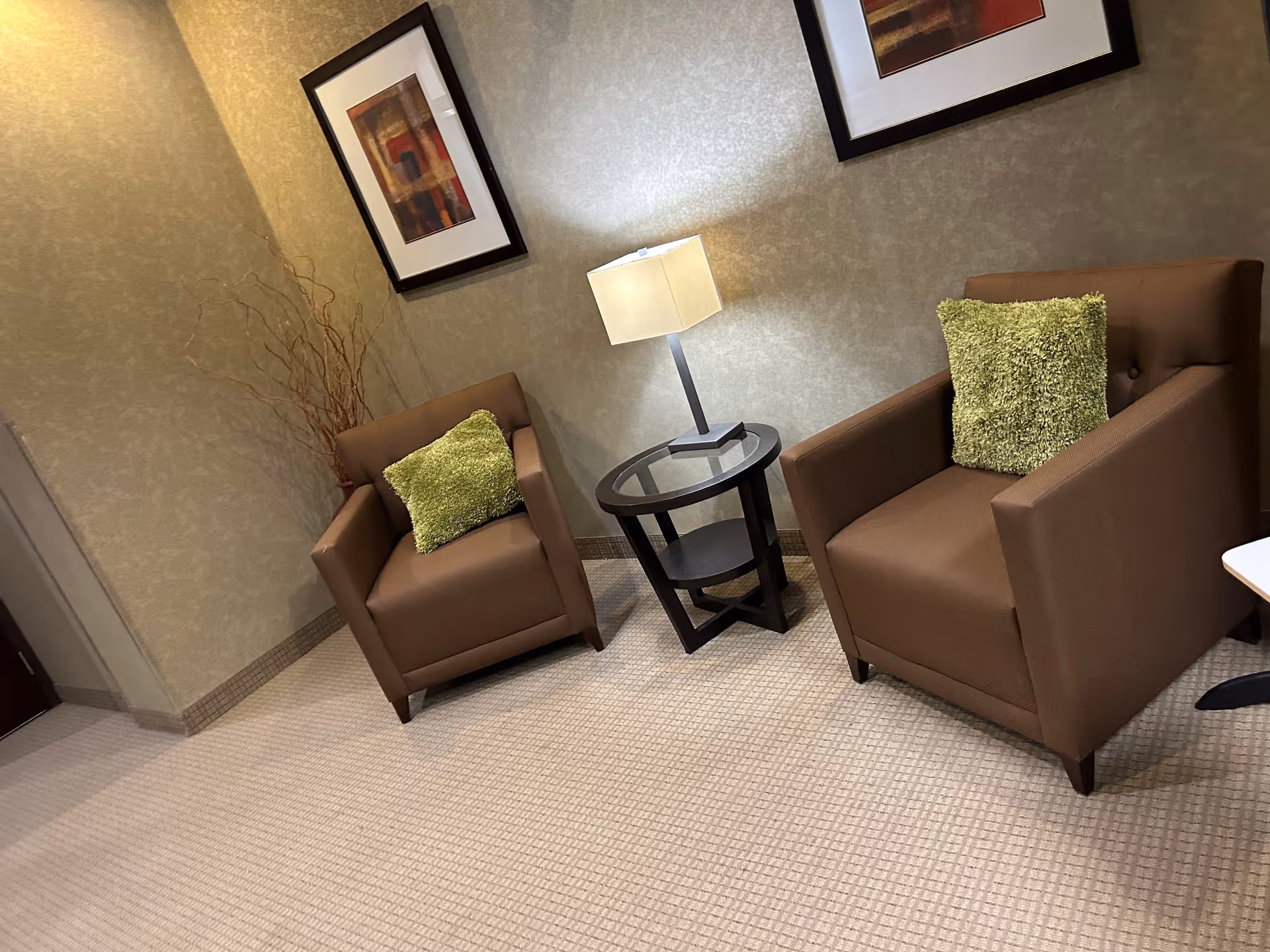 Two brown armchairs with green cushions, a lamp, and framed art in a cozy waiting area.