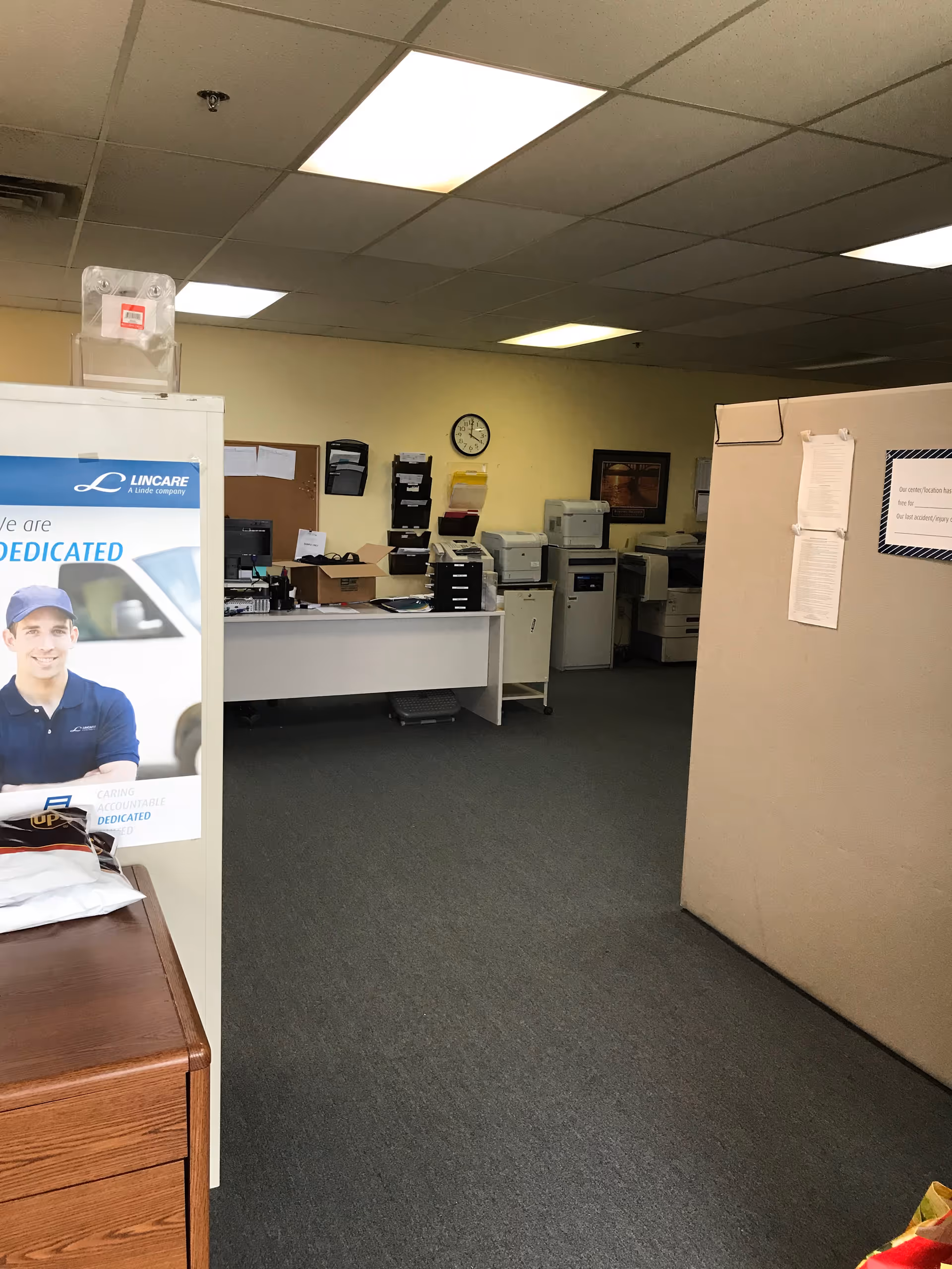 Interior office area with printers, cubicles, filing cabinets, and a Lincare poster.