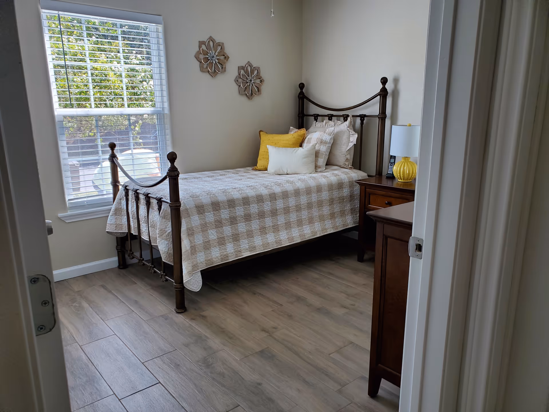 A neatly made bedroom with a metal bed frame, window view, and nightstand.