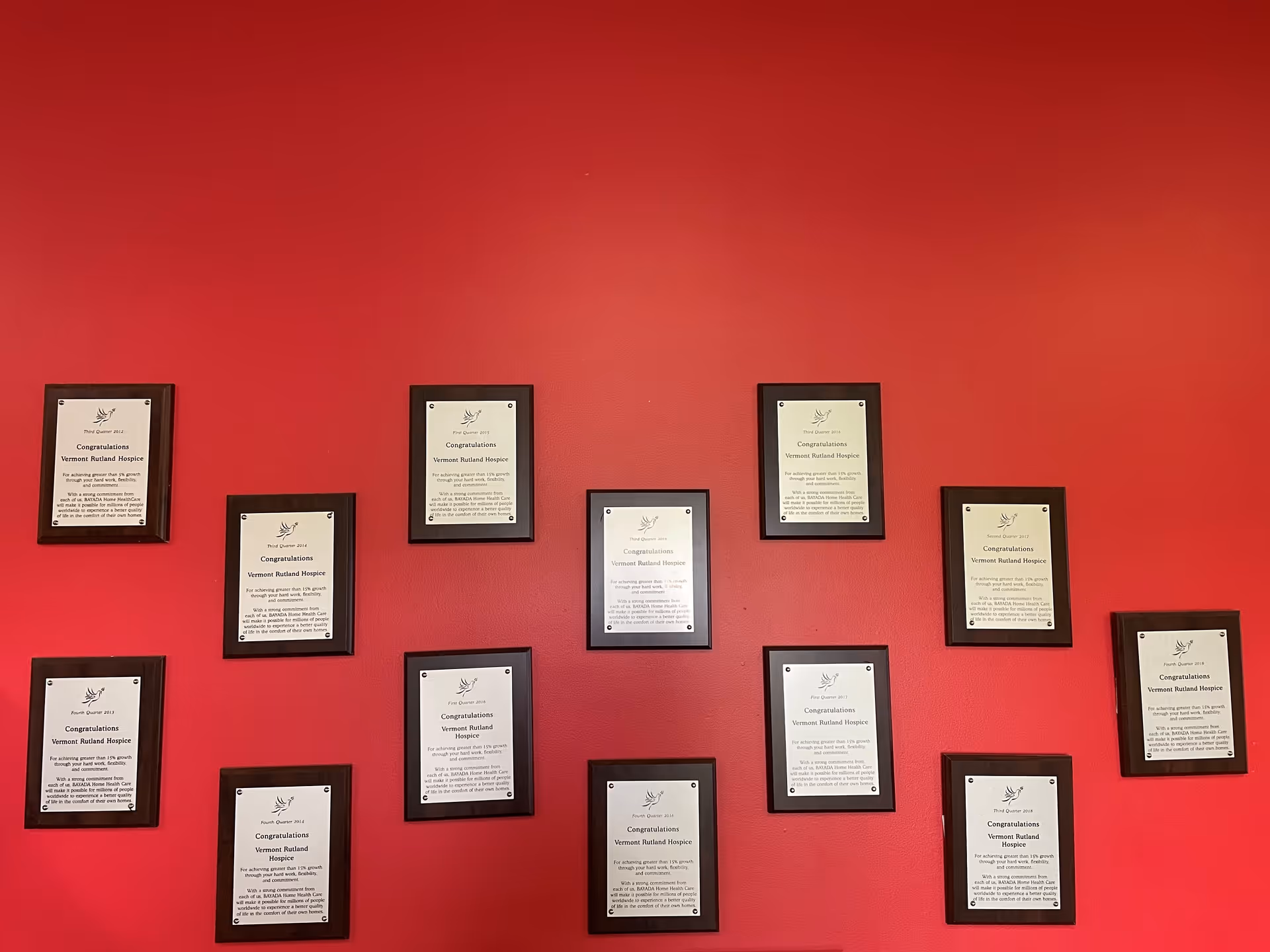 Red wall with multiple framed certificates arranged in a grid.
