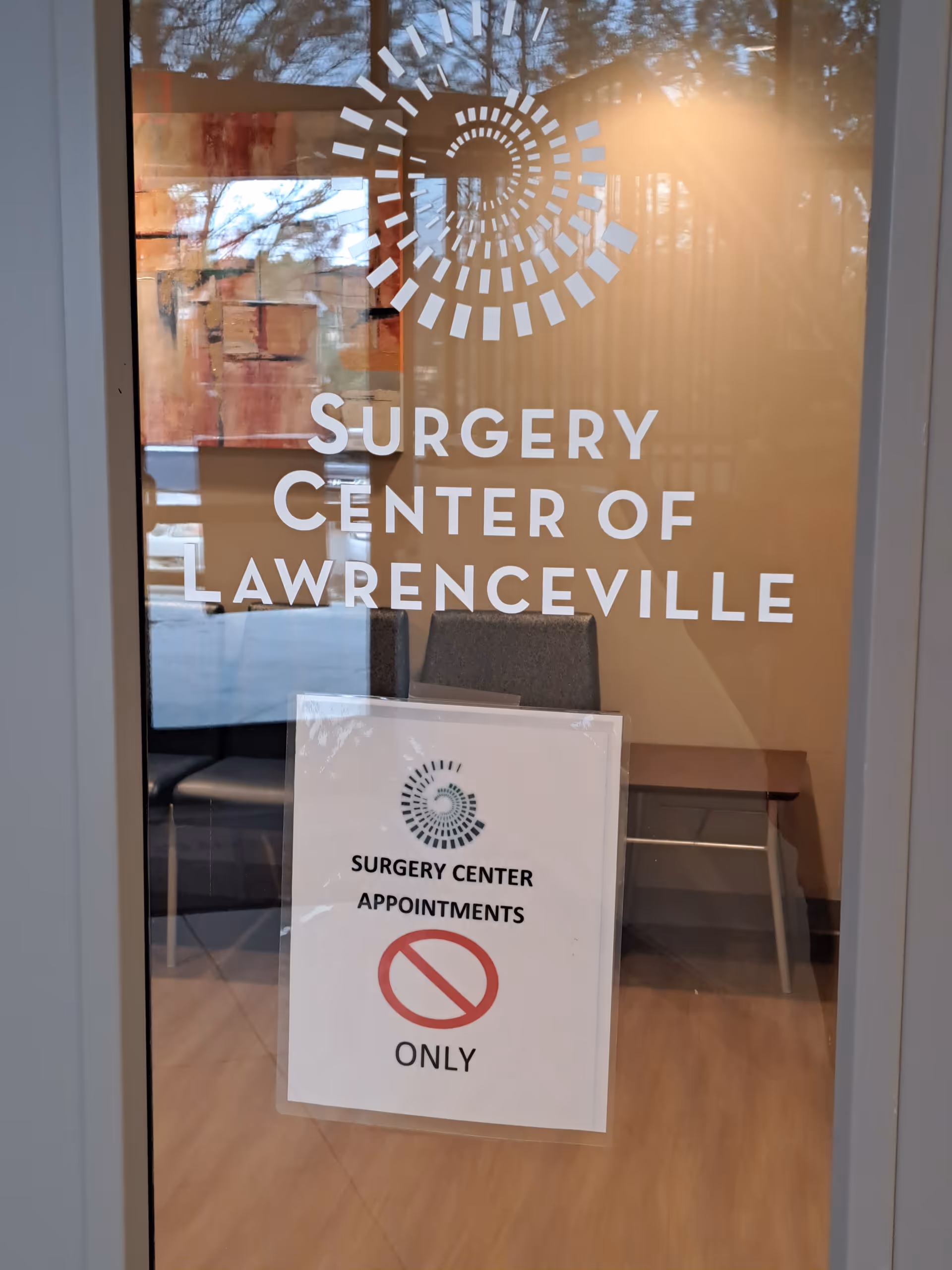 Glass door with Surgery Center of Lawrenceville signage and waiting chairs inside
