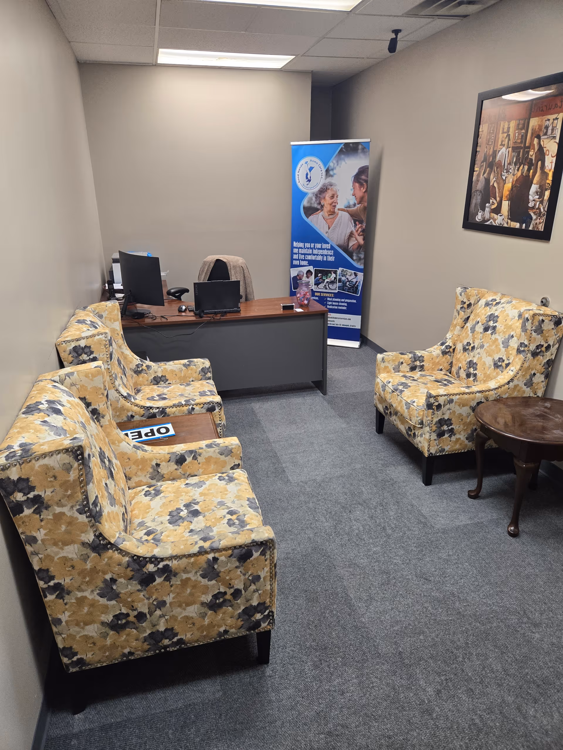 Interior office waiting area with floral upholstered chairs, desk, banner, and framed artwork.