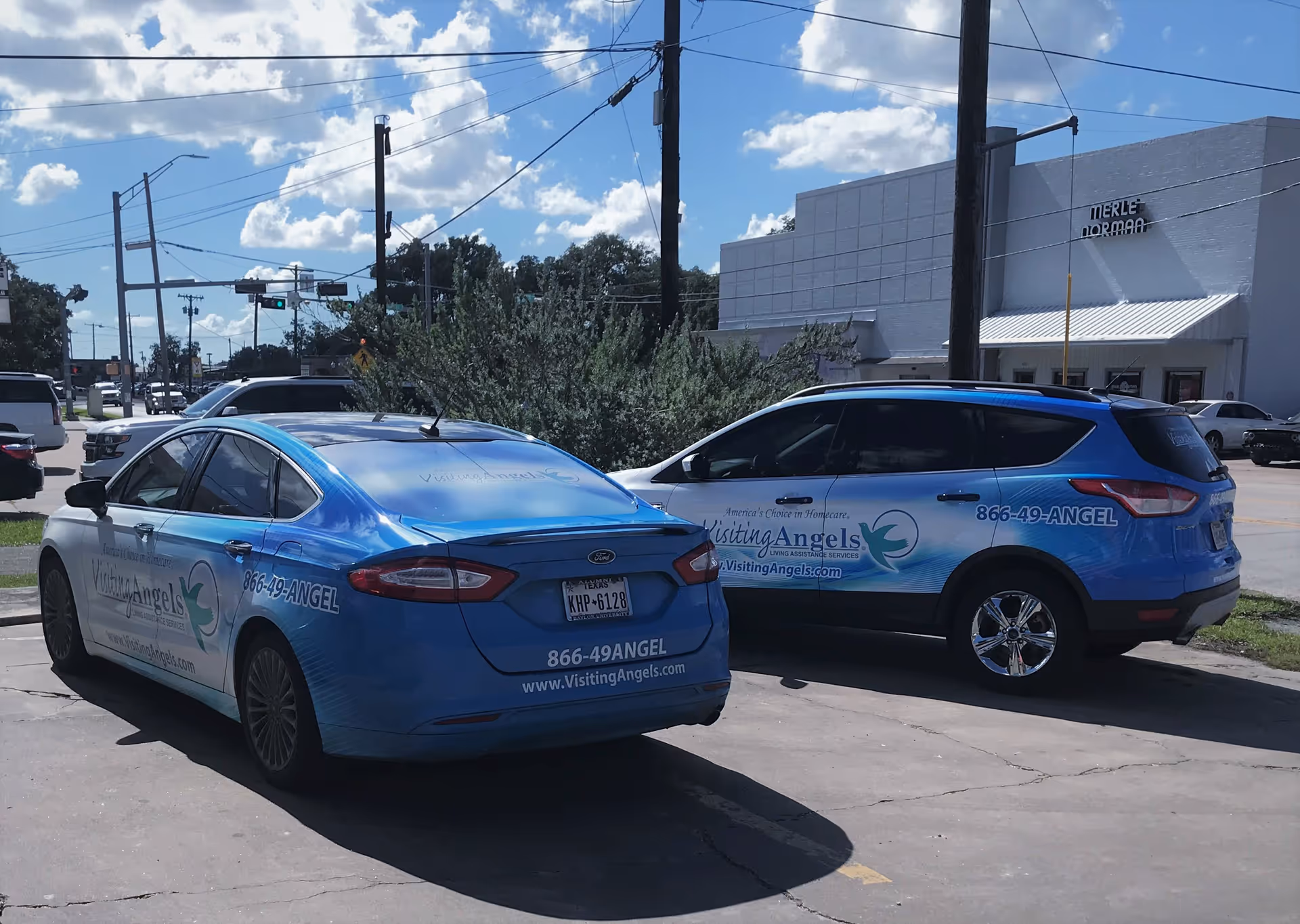 Two blue Visiting Angels vans parked outside a building on a sunny day
