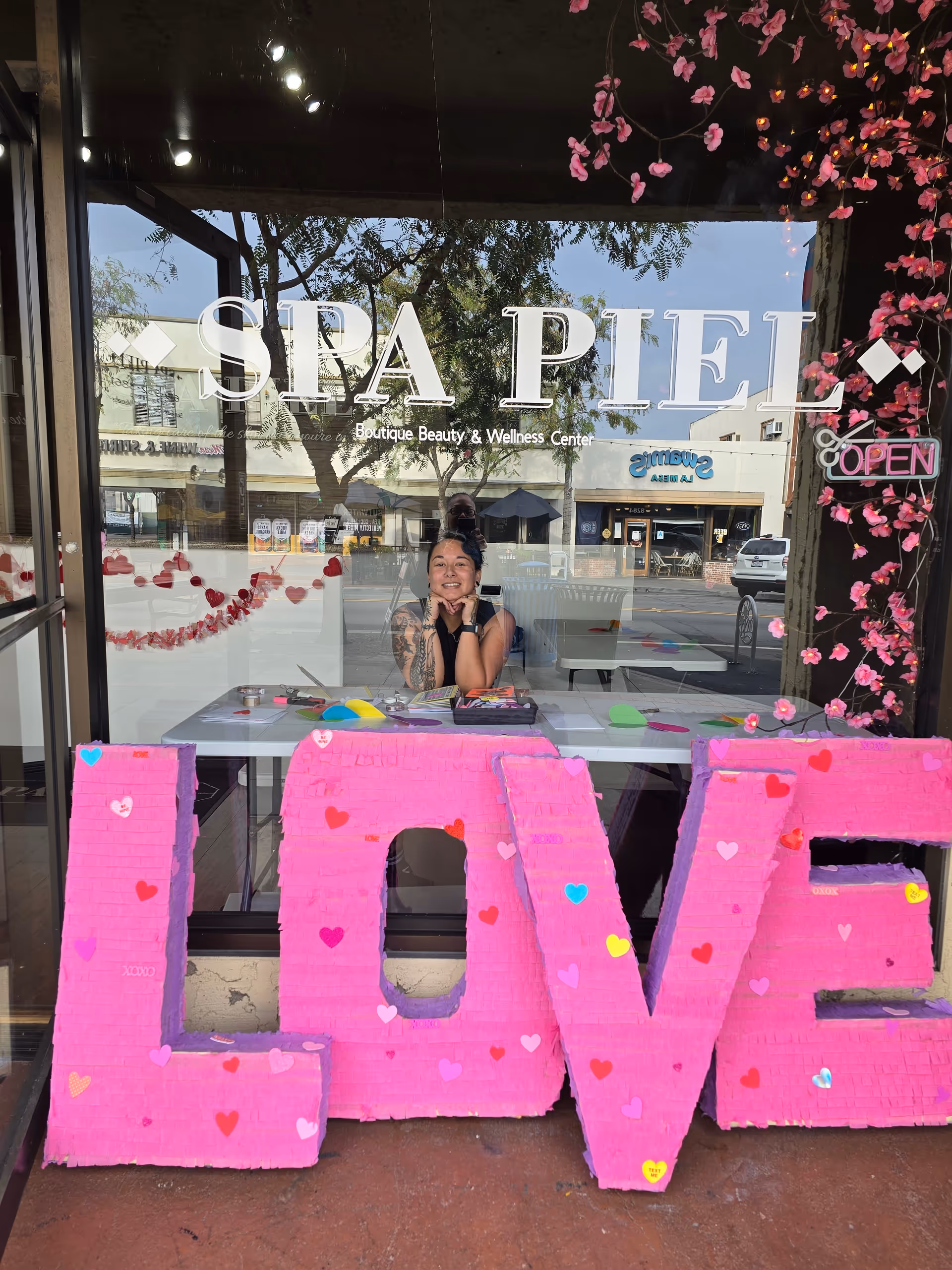 Storefront window with large pink LOVE letters outside and a person inside a spa.