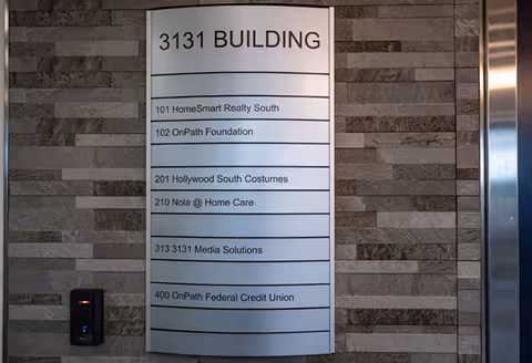 Wall-mounted directory sign in a building lobby lists tenants, including Nola @ Home Care.