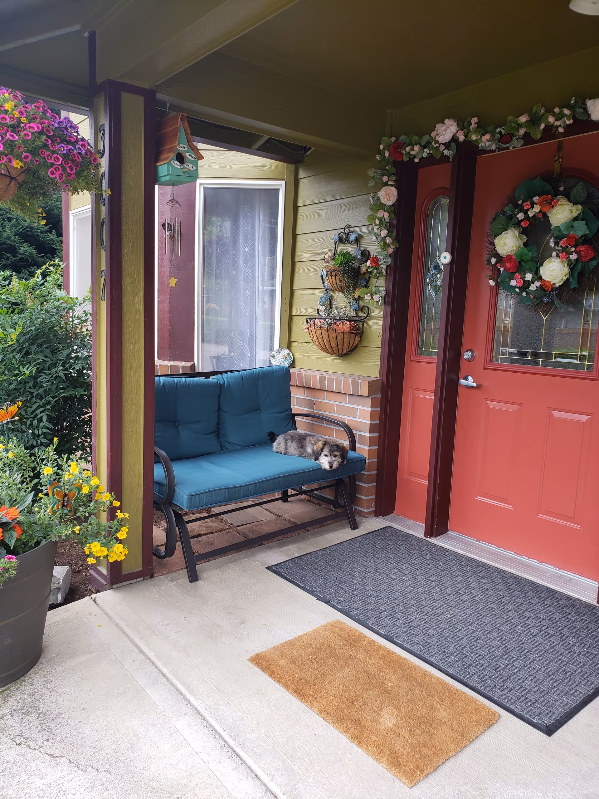 Front porch with teal cushioned bench, wreath, and dog resting near the red door.