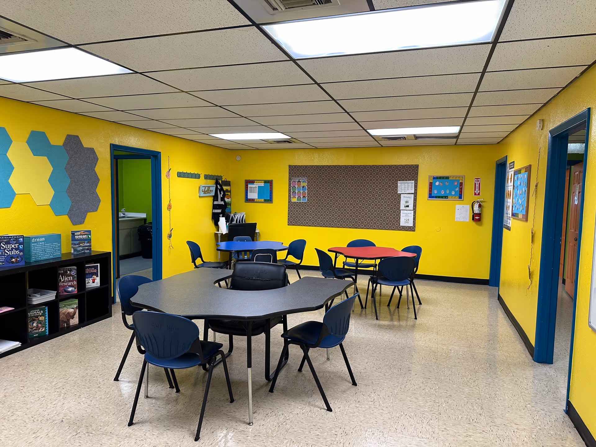 Bright yellow interior common area with round tables and blue chairs in a senior facility.